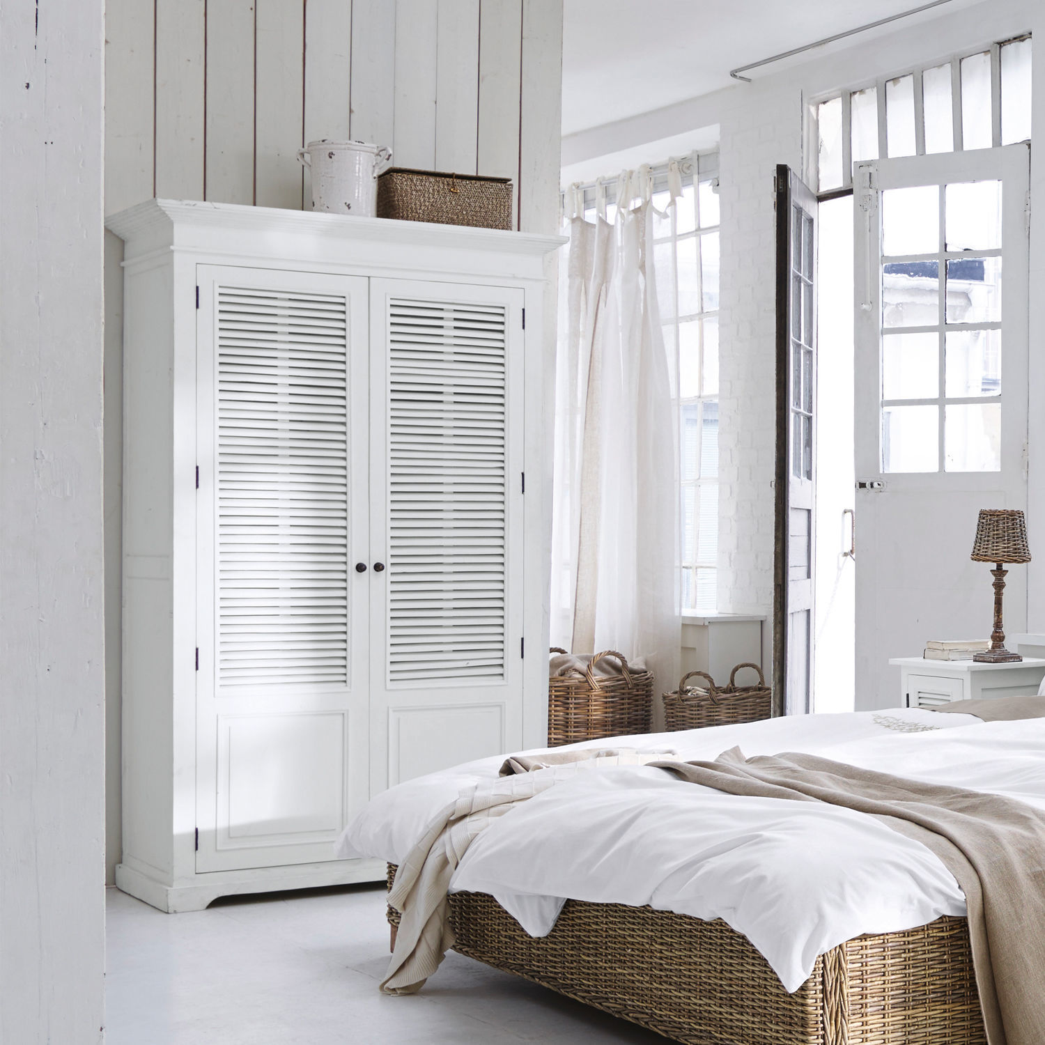 Weißer Holzschrank mit Lamellentüren in hellem Schlafzimmer mit Korbgeflecht-Bett