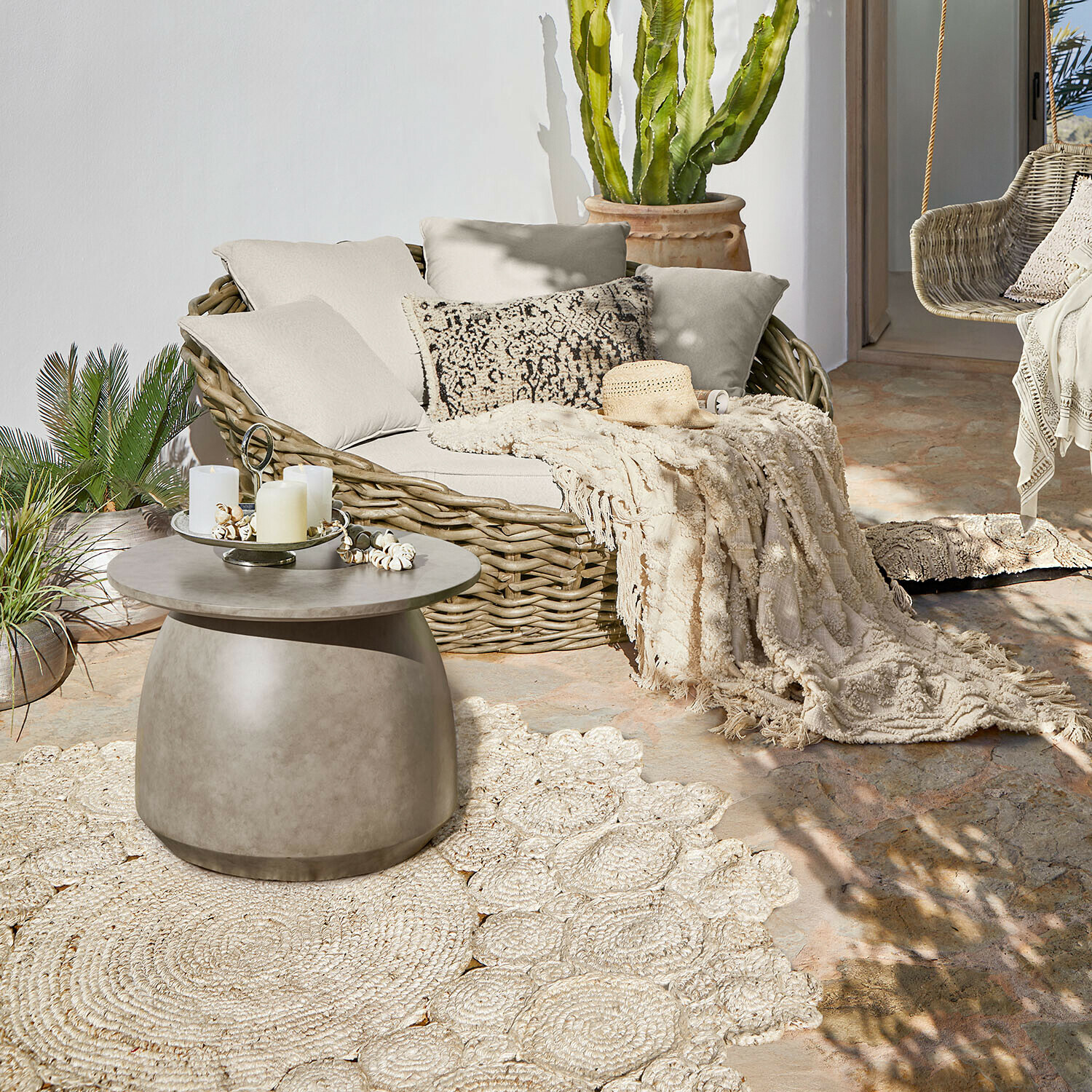 Runder Betontisch auf Terrasse mit Korbsofa und cremefarbenem dekorativem Plaid