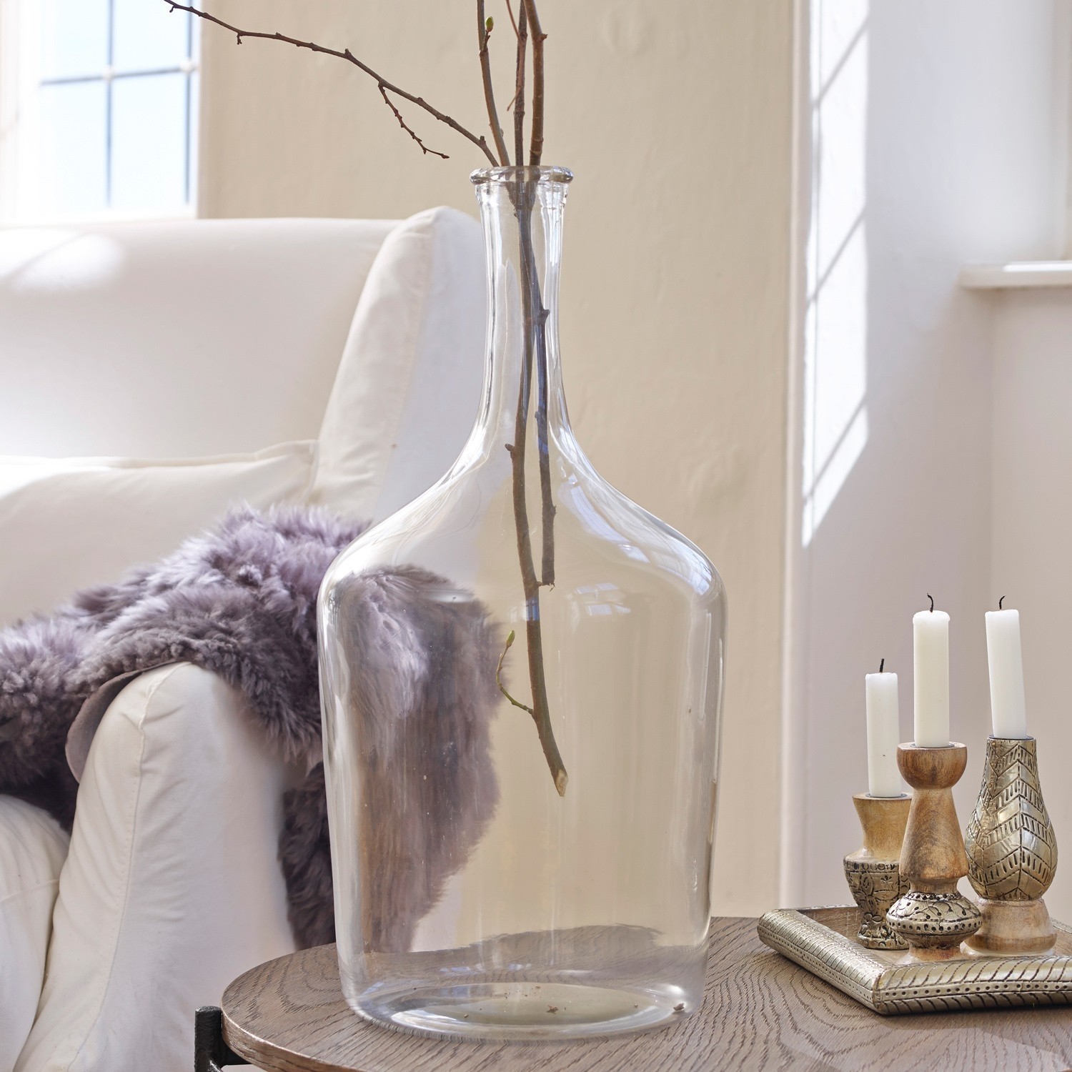 Transparente Glasvase mit Zweigen auf Holztisch im hellen Wohnzimmer mit weißem Sofa