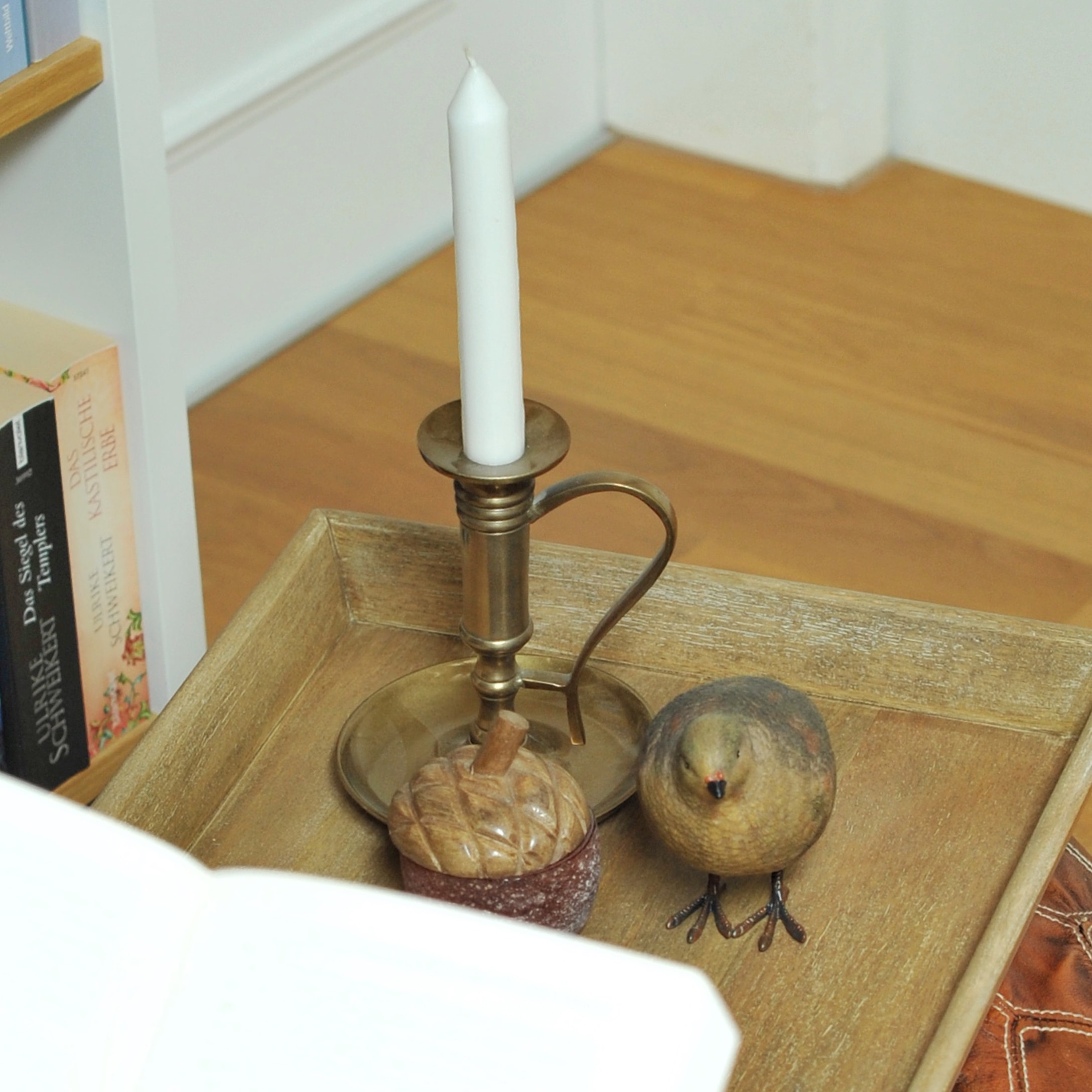 Metall-Kerzenhalter mit weißer Kerze und dekorativem Vogel auf Holztablett im Wohnzimmer