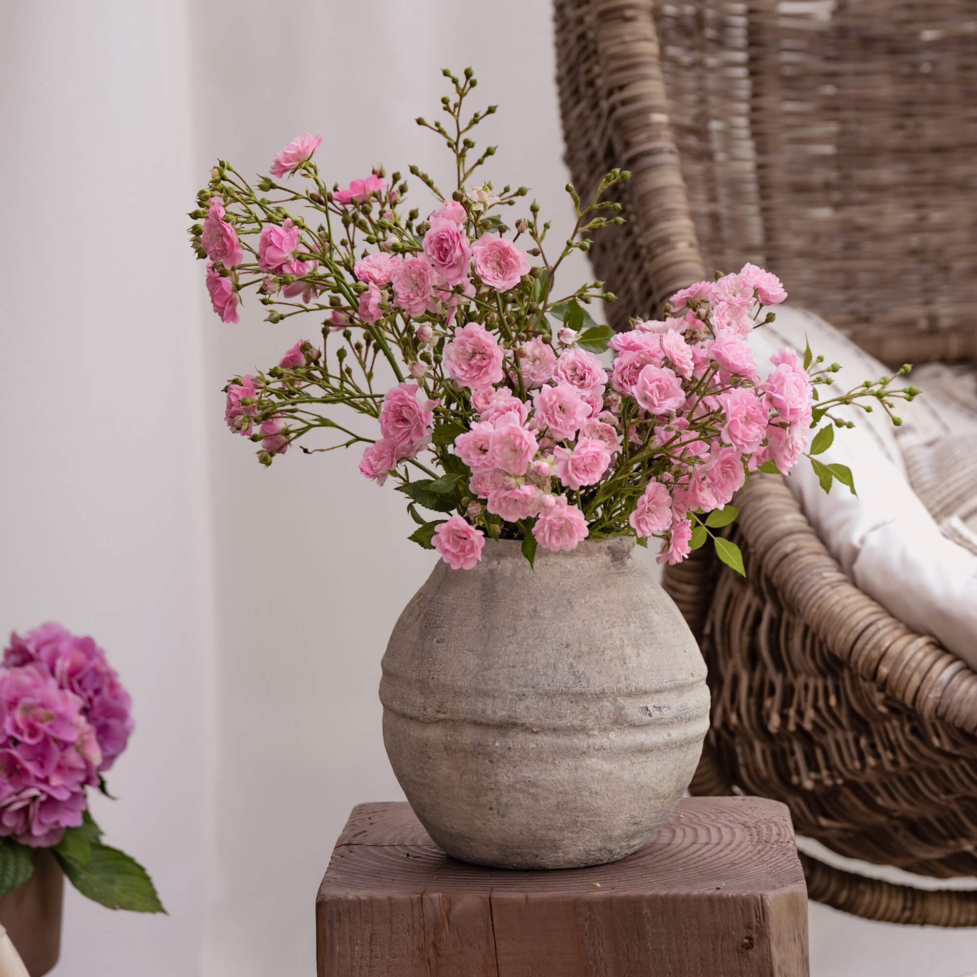 Grauer Keramikvase mit rosa Blumen auf Holzplatte in gemütlichem Raum