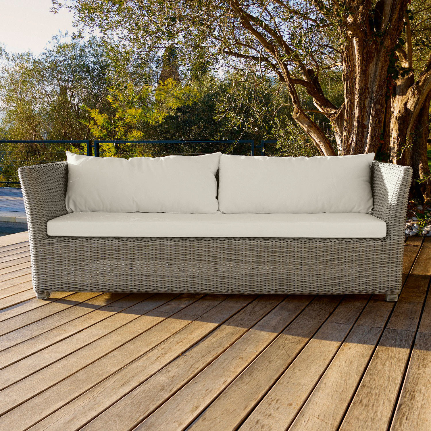 Gartensofa aus grauem Rattan mit cremefarbenen Kissen auf Holzterrasse, Outdoor-Möbel