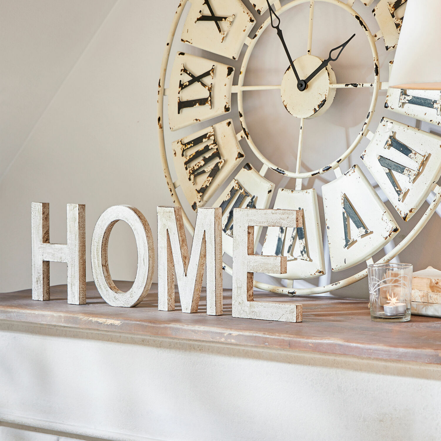 Dekorative weiße Holzbuchstaben HOME auf Kamin mit großer Vintage-Wanduhr im Hintergrund