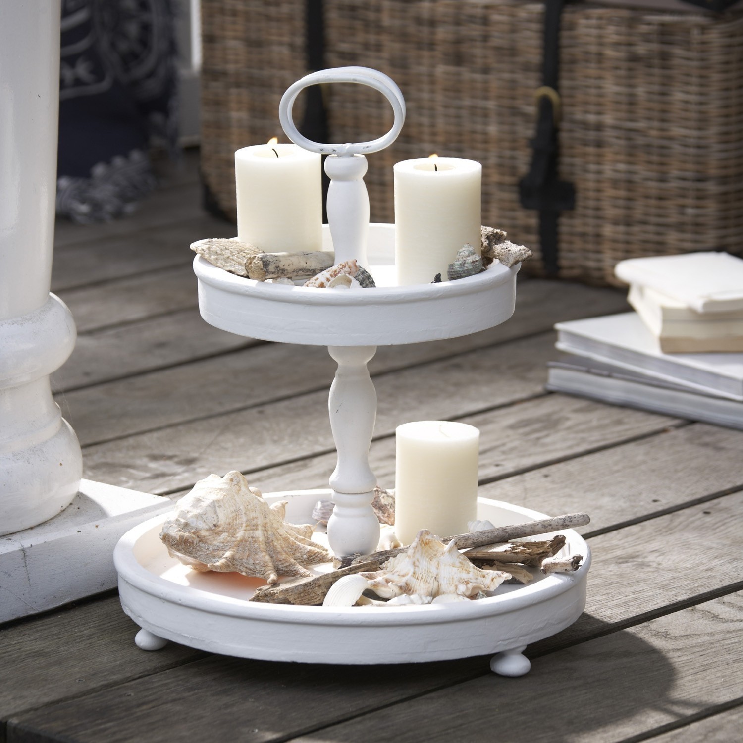 Weißer zweistöckiger Holzständer mit weißen Kerzen und Muscheln als Deko auf Terrasse