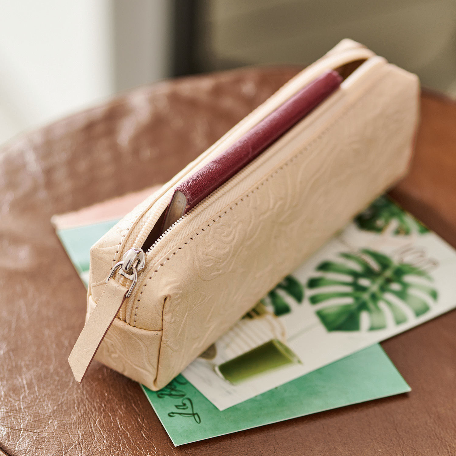 Beige Leder-Kosmetiktasche mit Prägung und Reißverschluss auf Tisch mit grünen Karten