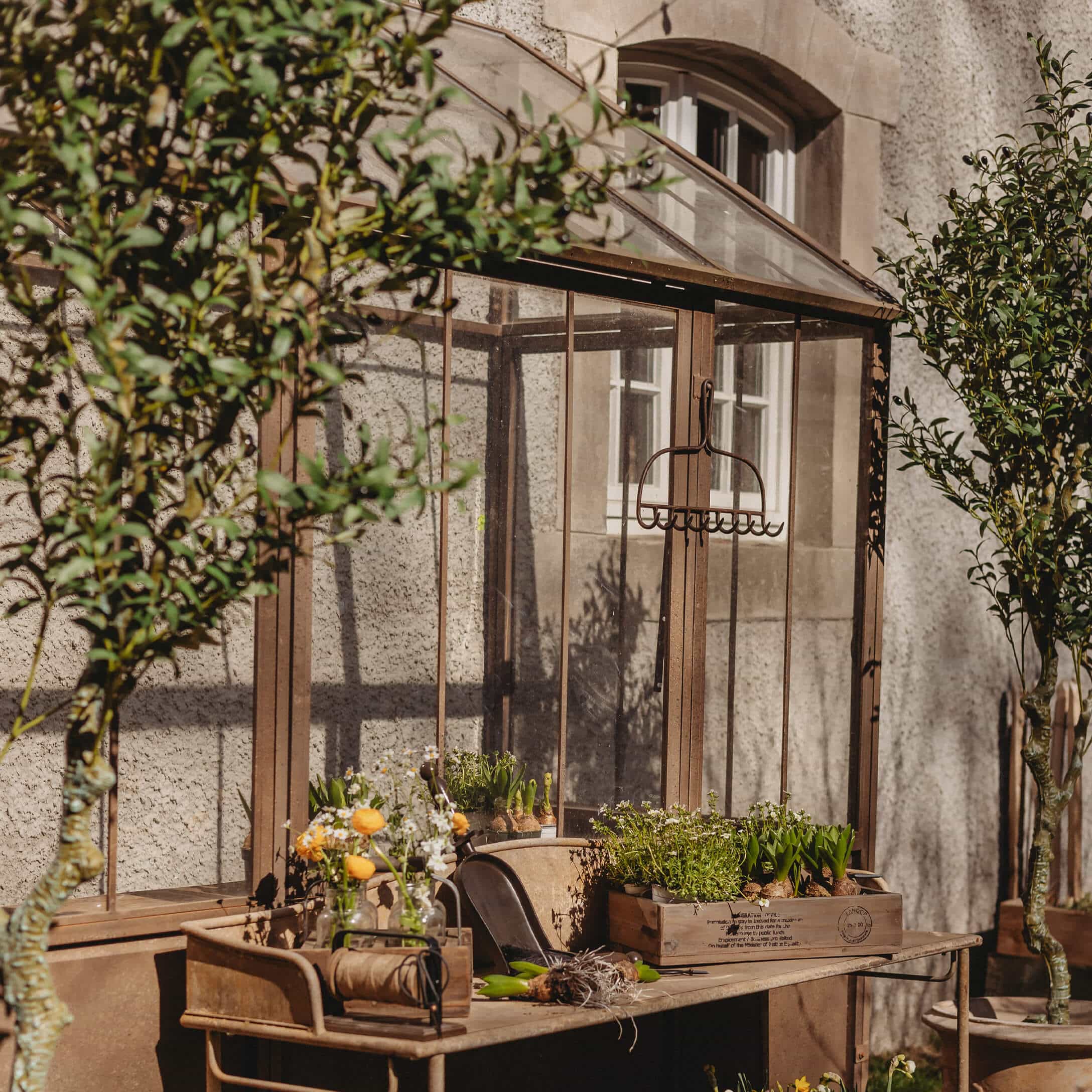 Vintage Metall-Gartentisch mit Blumentöpfen und Werkzeugen vor einem Glashaus