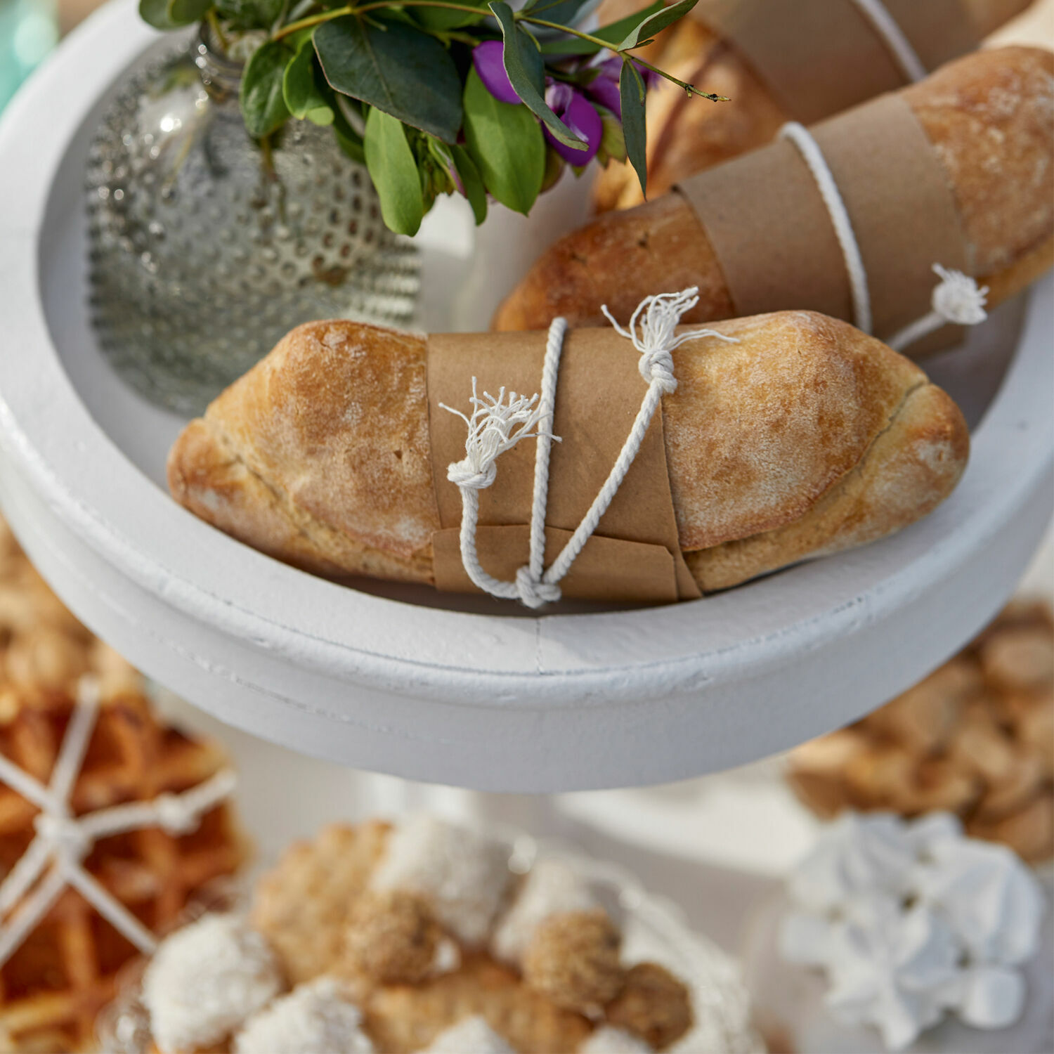 Frisches Brot in Papier und Schnur auf weißem Ständer mit Blumenarrangement dekoriert