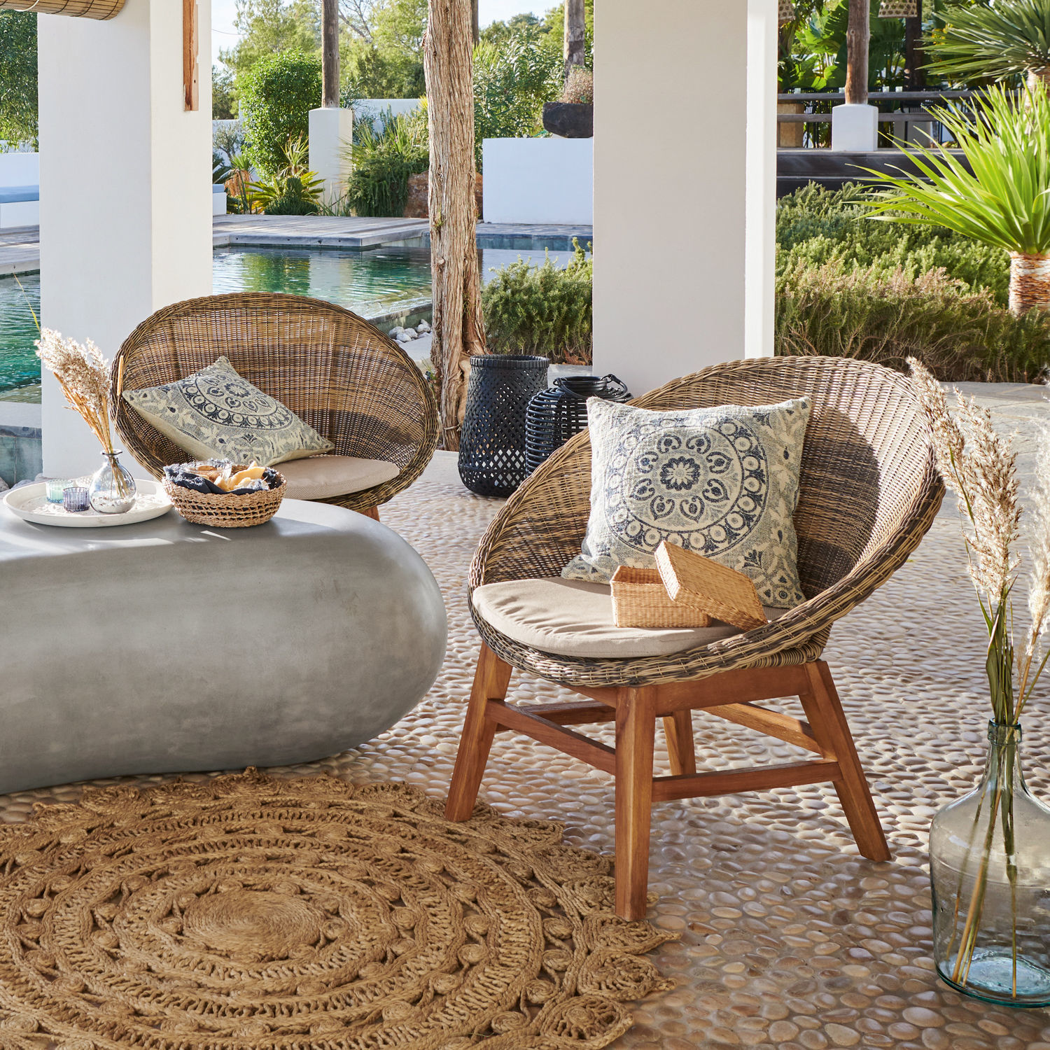 Set aus zwei Rattanstühlen mit Holzgestell und Kissen sowie Beton-Tisch auf Terrasse am Pool