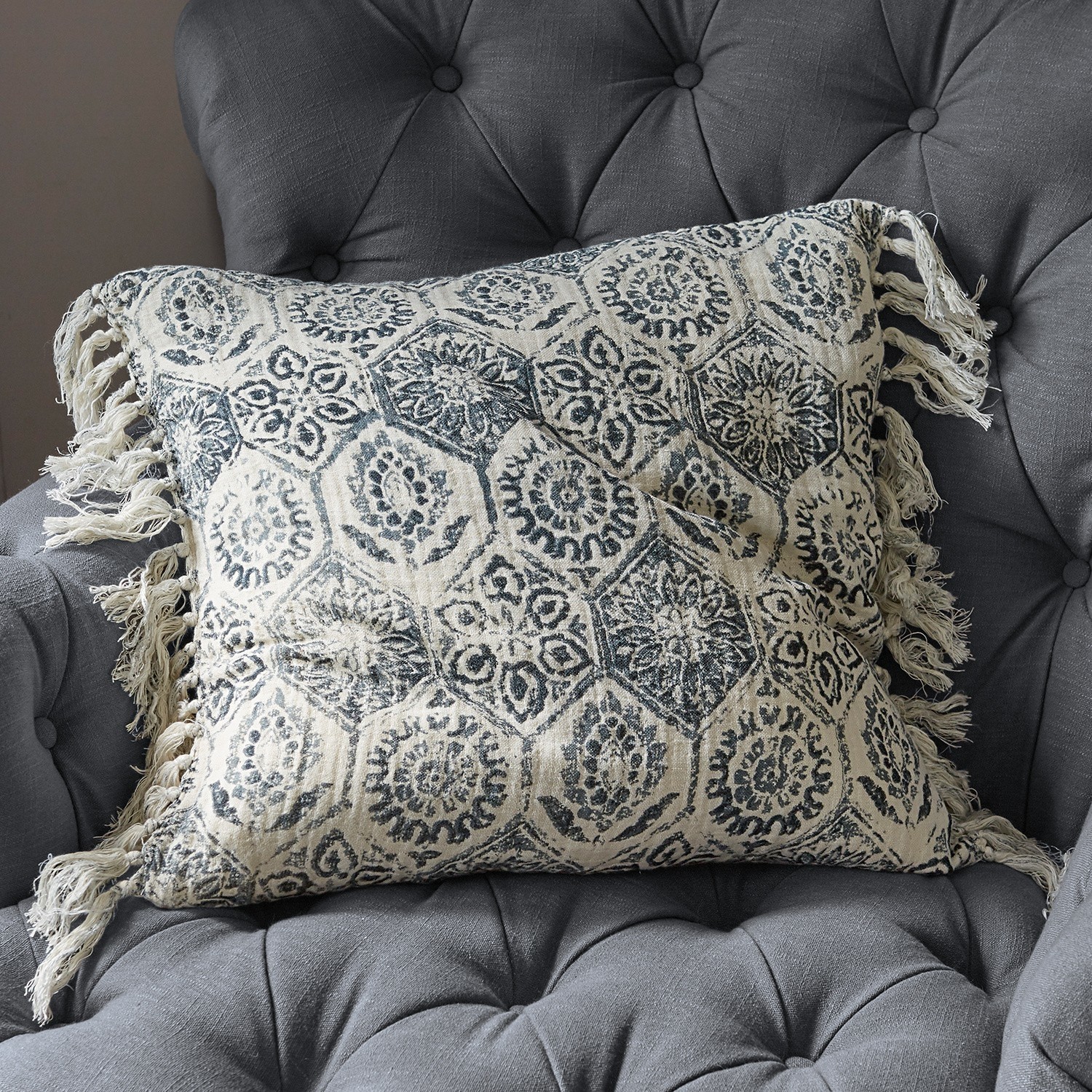 Beige Baumwollkissen mit blauem Muster und Fransen auf grauem, gepolstertem Sessel
