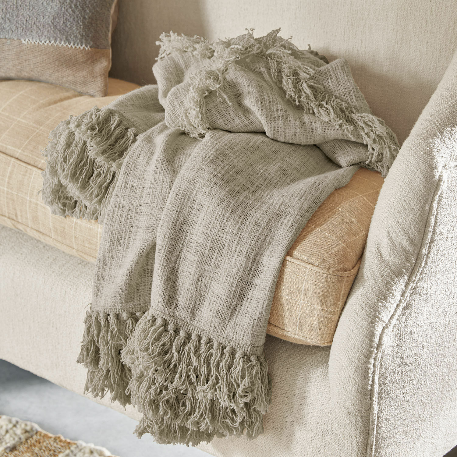 Plaid Freya Beige Fransen-Plaid aus weichem Material auf hellem Sofa, gemütliche Wohnraumdekoration