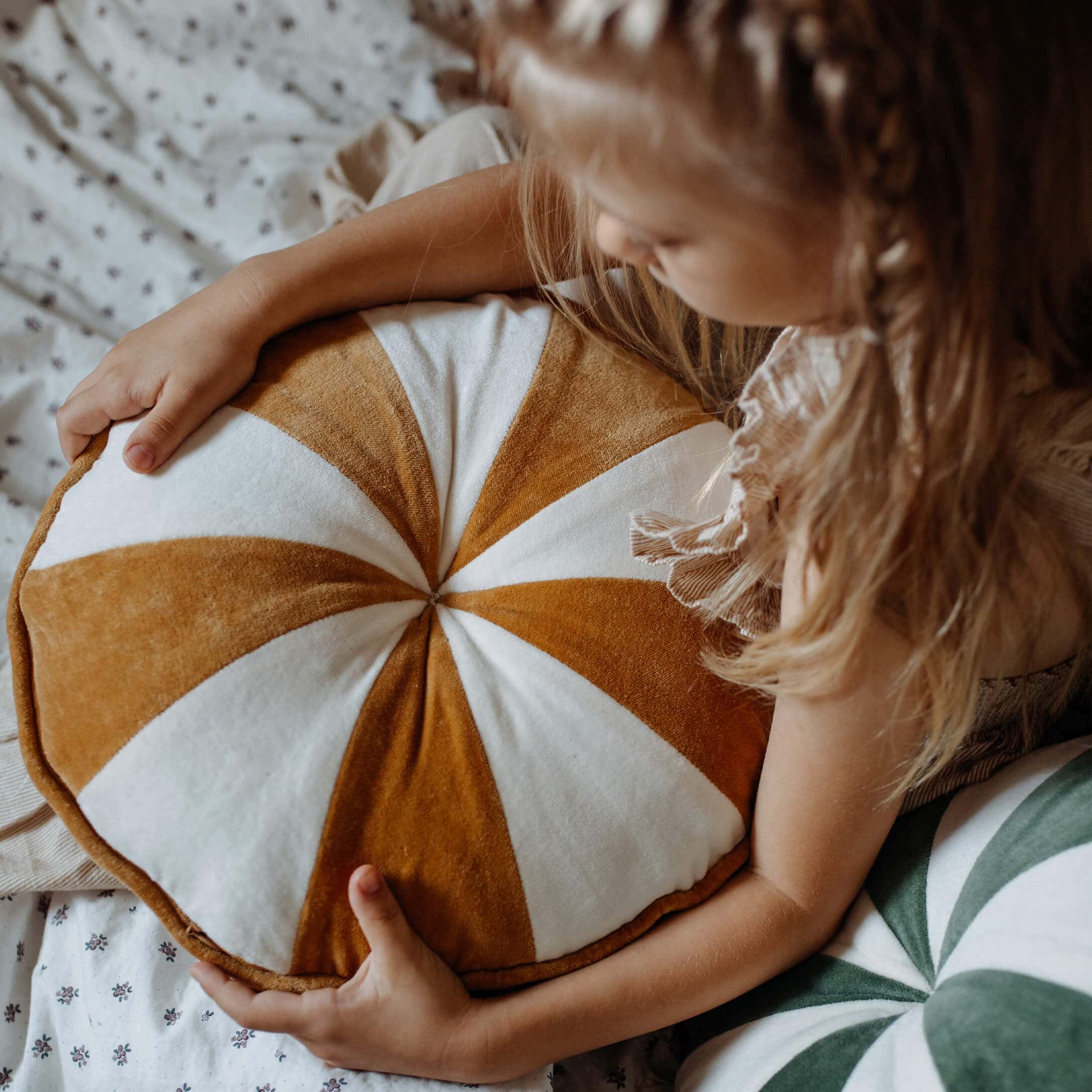 Kind hält runde Kissen mit braun-weißen Streifen aus weichem Material für Kinderzimmer