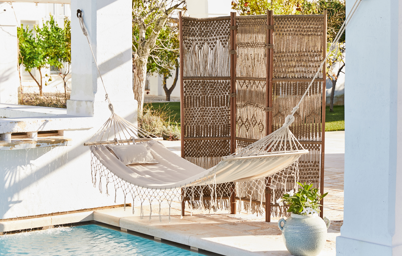 Beiger Stoff-Hängematte mit Kissen und geflochtenem Paravent auf Terrasse am Pool im Boho-Stil