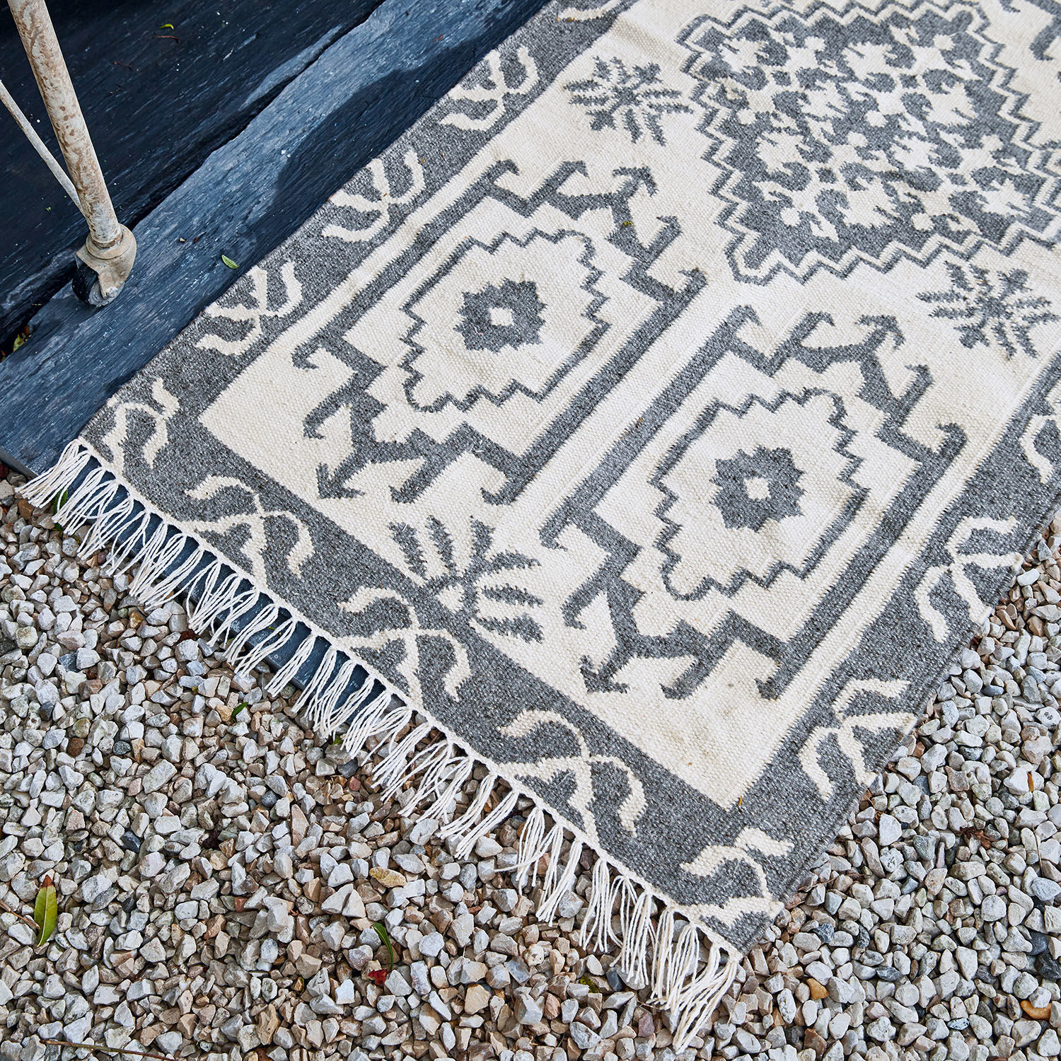 Baumwollteppich in Grau-Weiß mit geometrischem Muster und Fransen auf Kiesboden