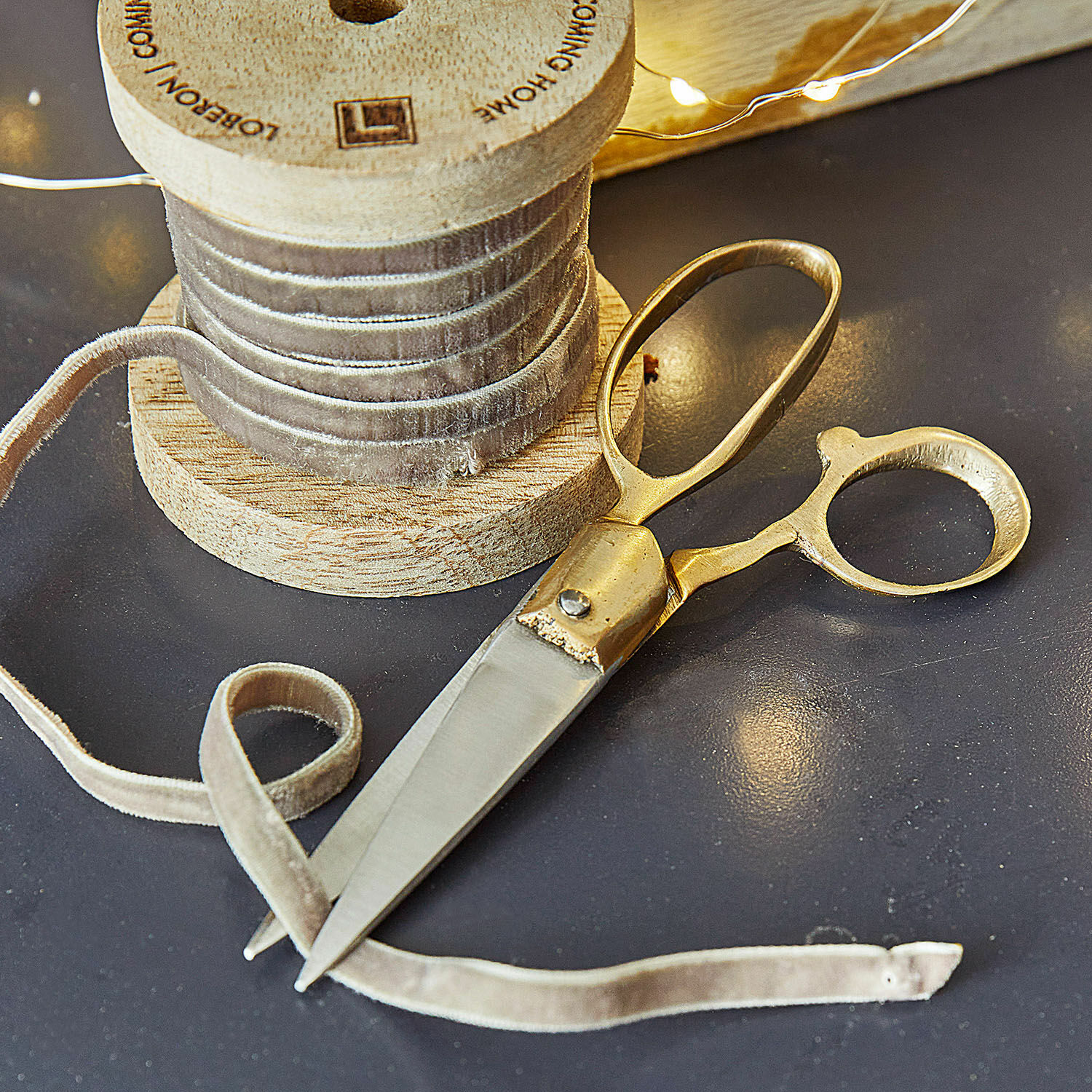 Schere Sterre Goldene Schere und beiges Samtband auf Holzspule auf dunklem Tisch für Dekoration und Nähen