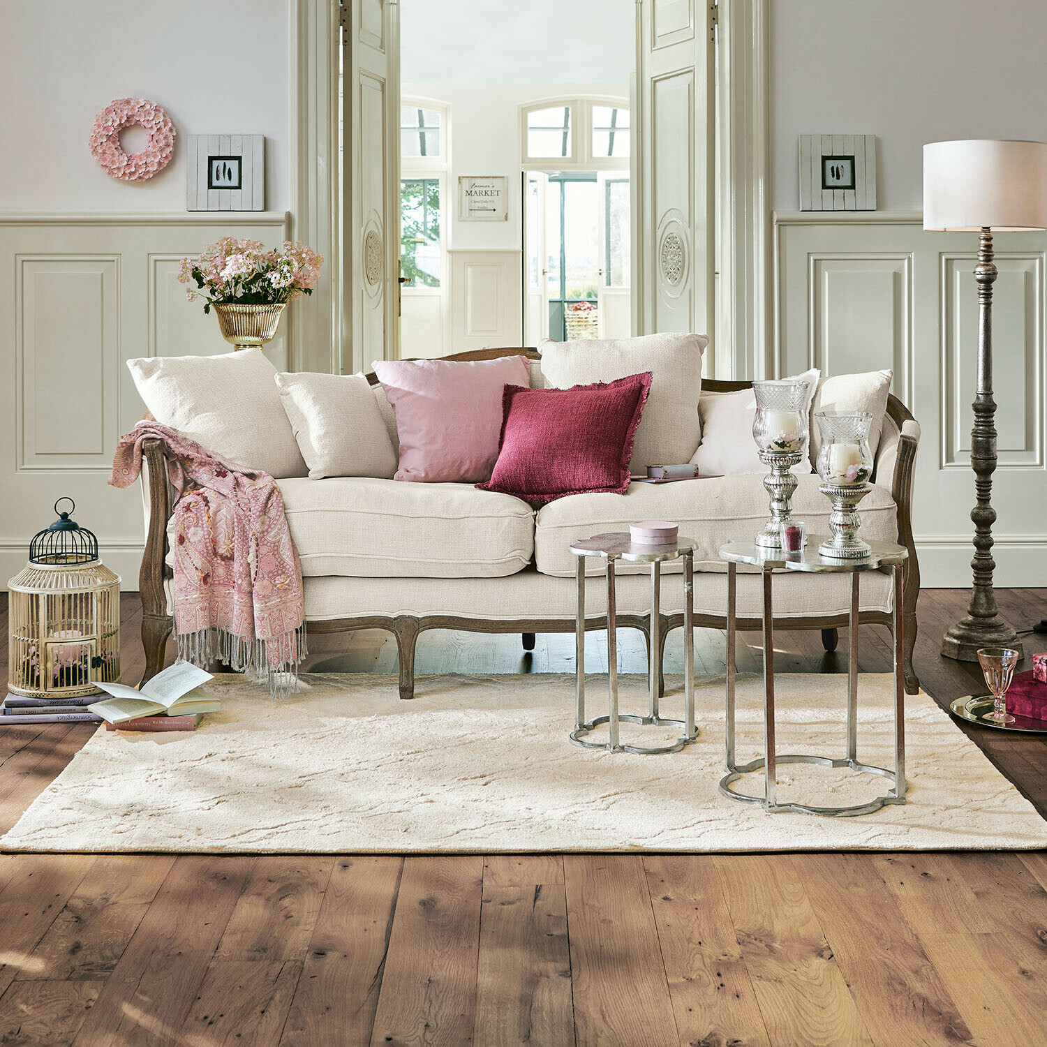 Beiges Sofa mit Holzrahmen und rosa Kissen in elegantem Wohnzimmer mit Teppich und Beistelltischen