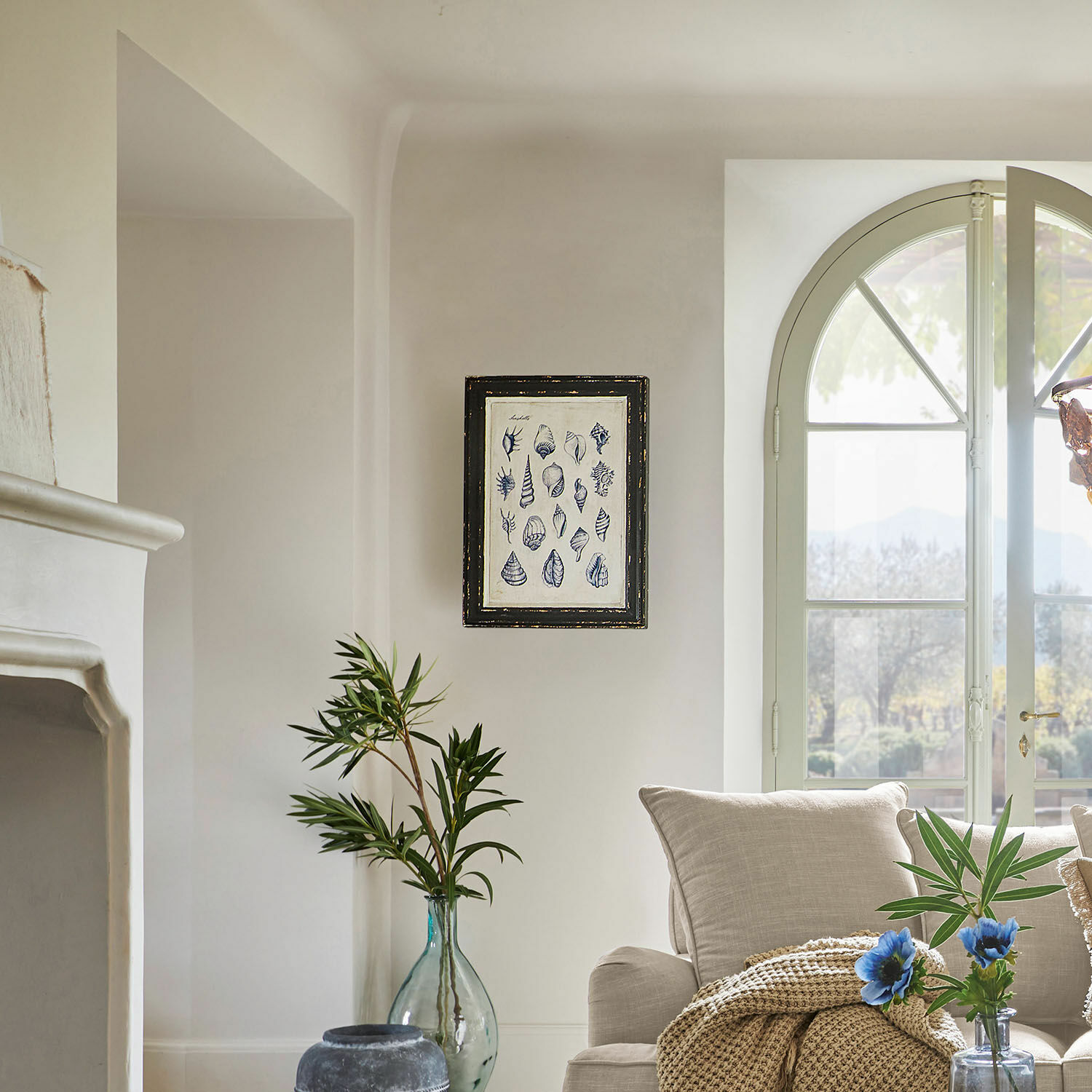 Helles Wohnzimmer mit beigem Sofa, grünen Pflanzen und gerahmtem Muschelbild an der Wand