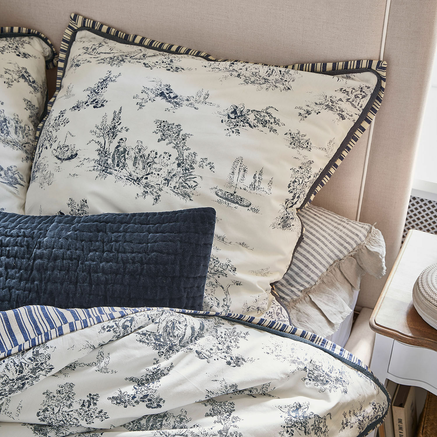 Bettwäsche aus Baumwolle in Creme mit blauem Muster und Streifen, dekorative Kissen auf dem Bett