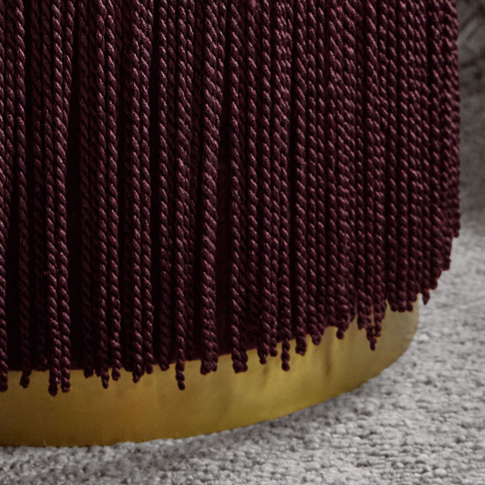 Bordeauxfarbener, gedrehter Stoff auf gelbem Untergrund auf grauem Teppich, textile Struktur