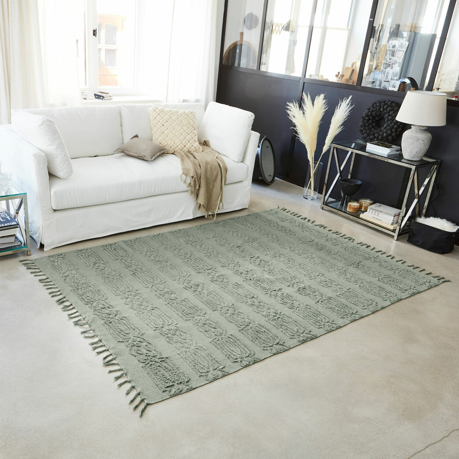 Weicher grüner Baumwollteppich mit dekorativem Muster und Fransen im modernen Wohnzimmer mit weißem Sofa