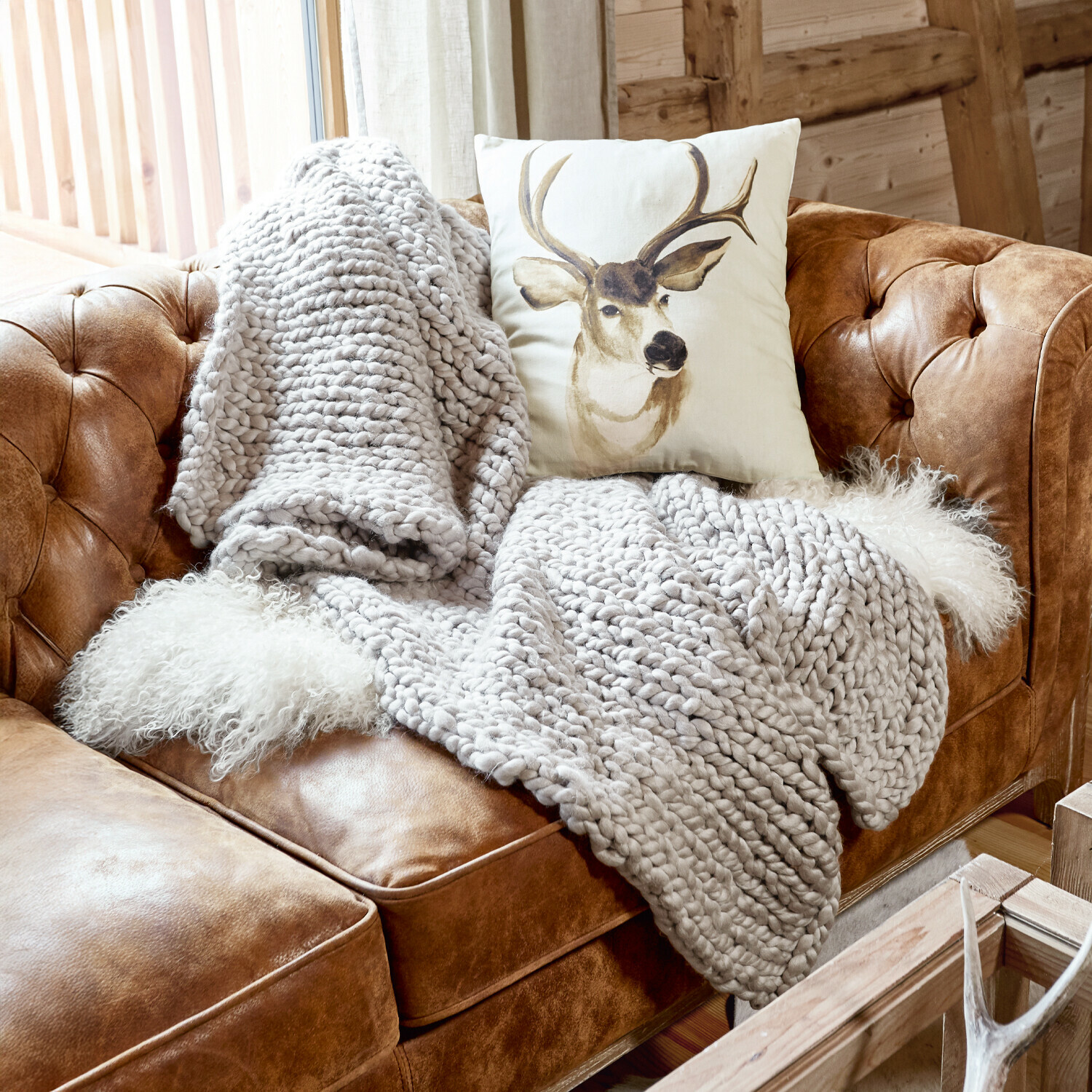 Plaid Reidous Braunes Ledersofa mit grob gestrickter grauer Decke und Hirschmotiv-Kissen in rustikalem Raum