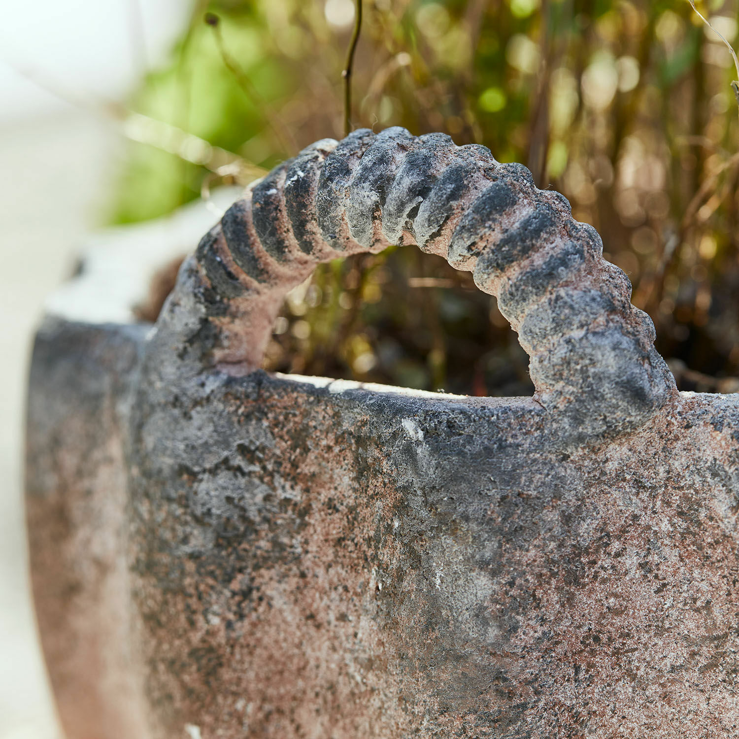 Nahaufnahme eines rostigen, steinernen Griffs eines Gartentopfes mit rauer Oberfläche