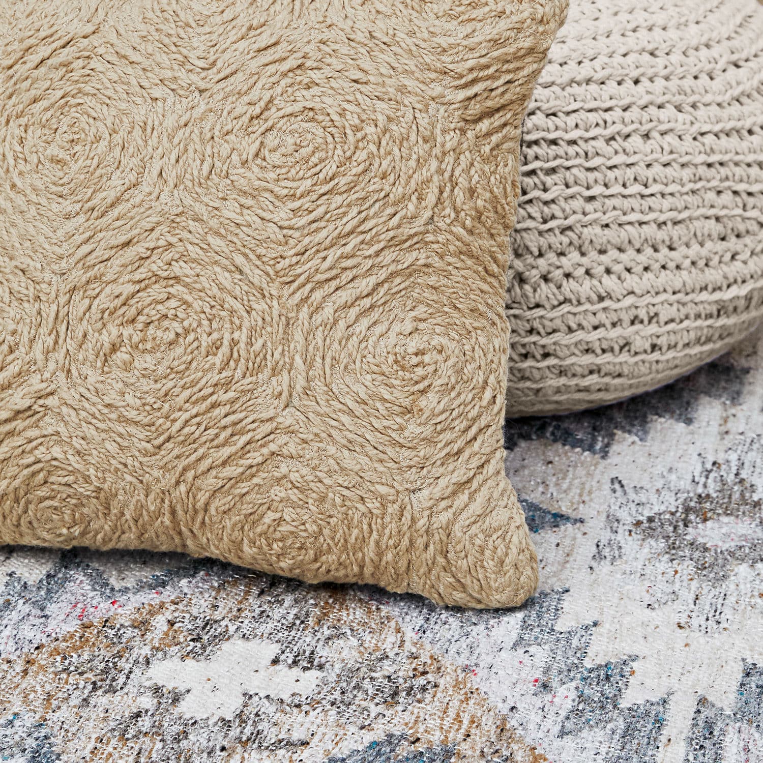 Beige dekoratives Kissen aus natürlichem Material mit geflochtenem Muster auf gemustertem Teppich