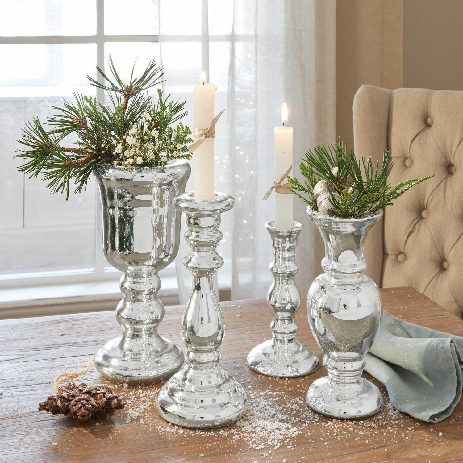 Silberne Glas-Kerzenhalter und Vasen mit grünen Zweigen auf Holztisch, festliche Dekoration
