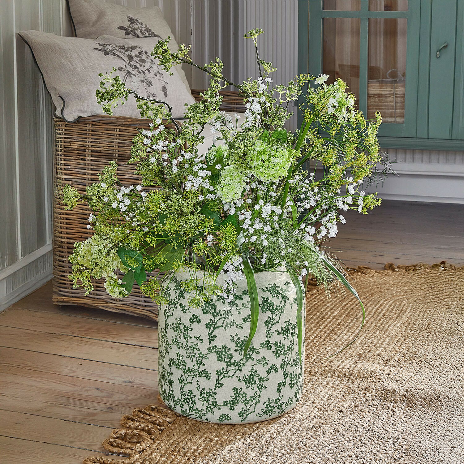 Vase Vaudrisse Weiße Keramikvase mit grünem Muster, gefüllt mit weißen und grünen Blumen auf Holzboden