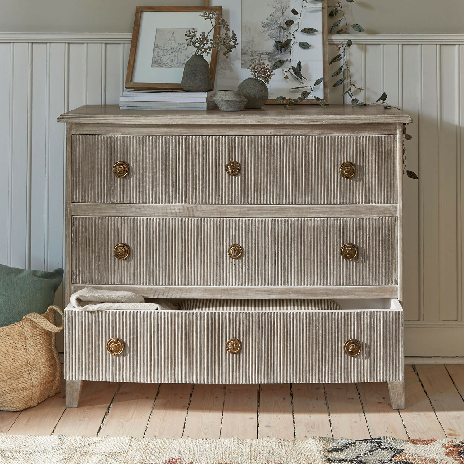 Kommode Boissiére Kommode aus geriffeltem Holz in Beige mit Messinggriffen und Dekorationen auf der Ablage