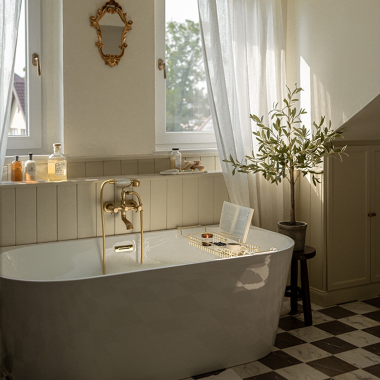 Weiße freistehende Badewanne mit Messingarmatur und dekorativem Spiegel in hellem Badezimmer mit Pflanze