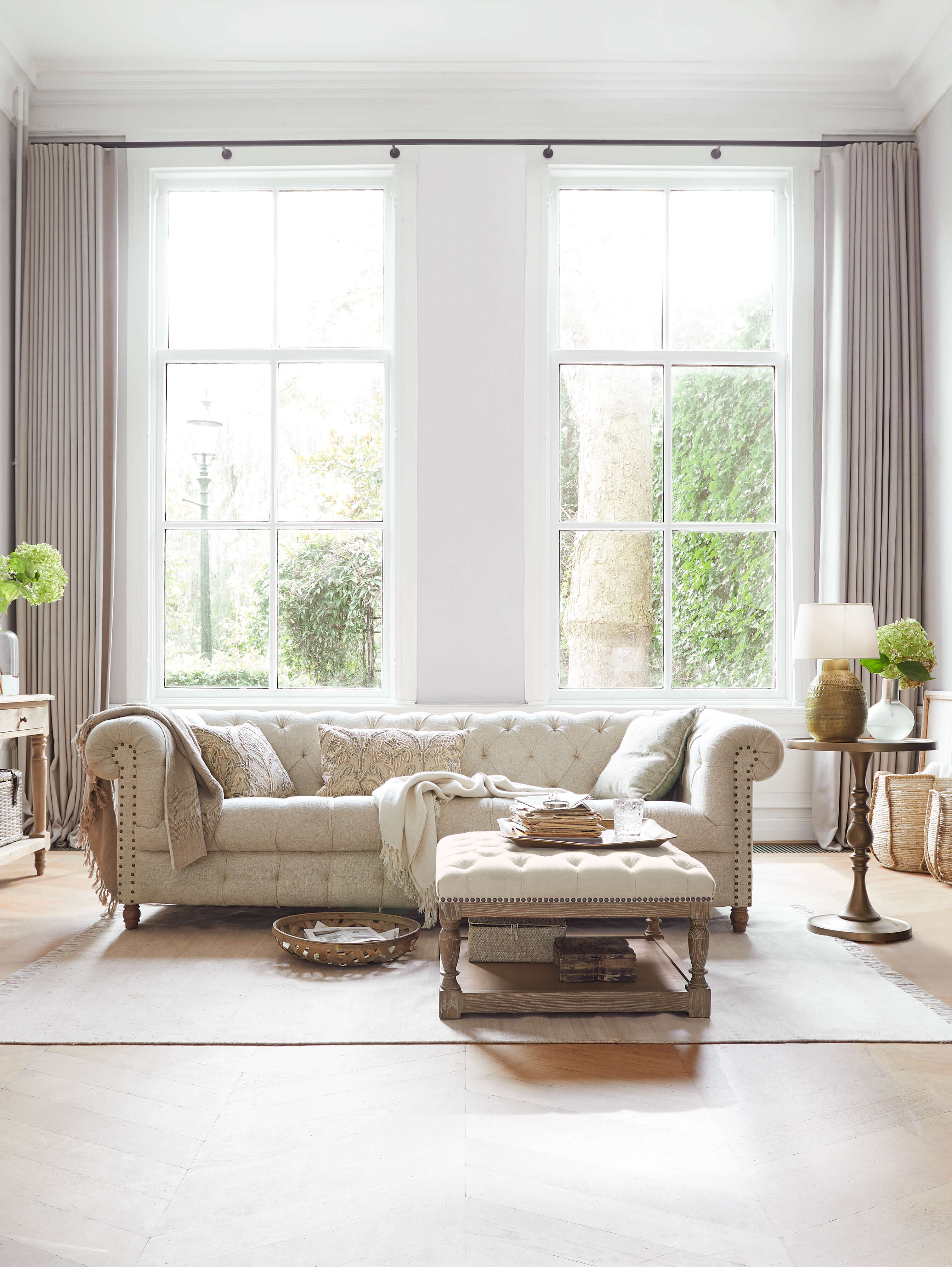 Beige gepolstertes Chesterfield-Sofa aus Stoff in hellem Wohnzimmer mit natürlichem Licht