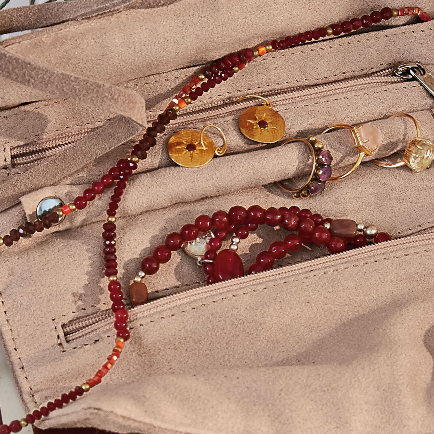 Beiger Wildleder-Schmuckorganizer mit roten Perlen und goldfarbenen Ringen