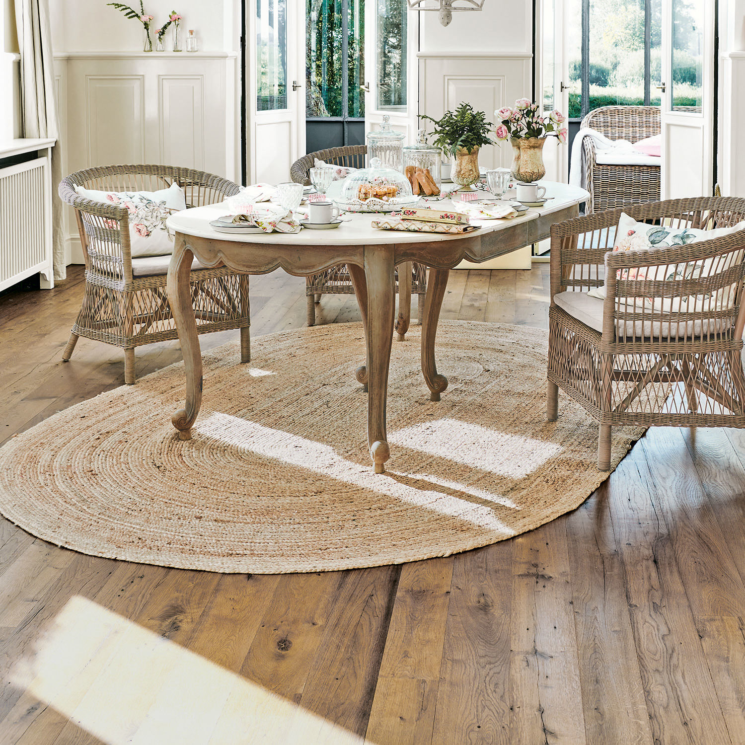 Teppich Ausone Heller Holztisch mit weißer Tischplatte auf rundem Jute-Teppich in hellem Raum mit Rattanstühlen