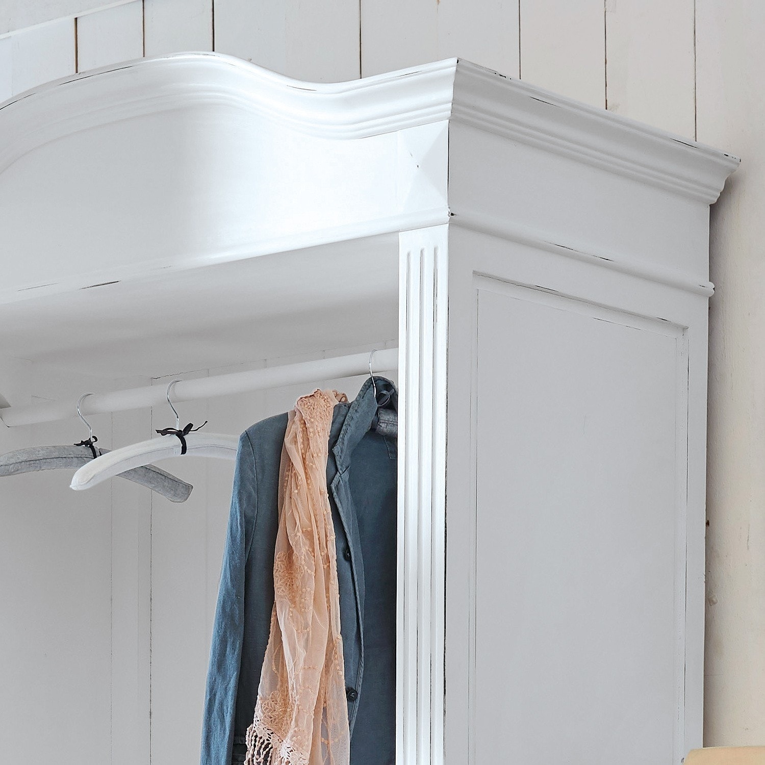 Weißer Holzkleiderschrank mit dekorativem oberen Abschluss und Kleidung an Kleiderbügeln