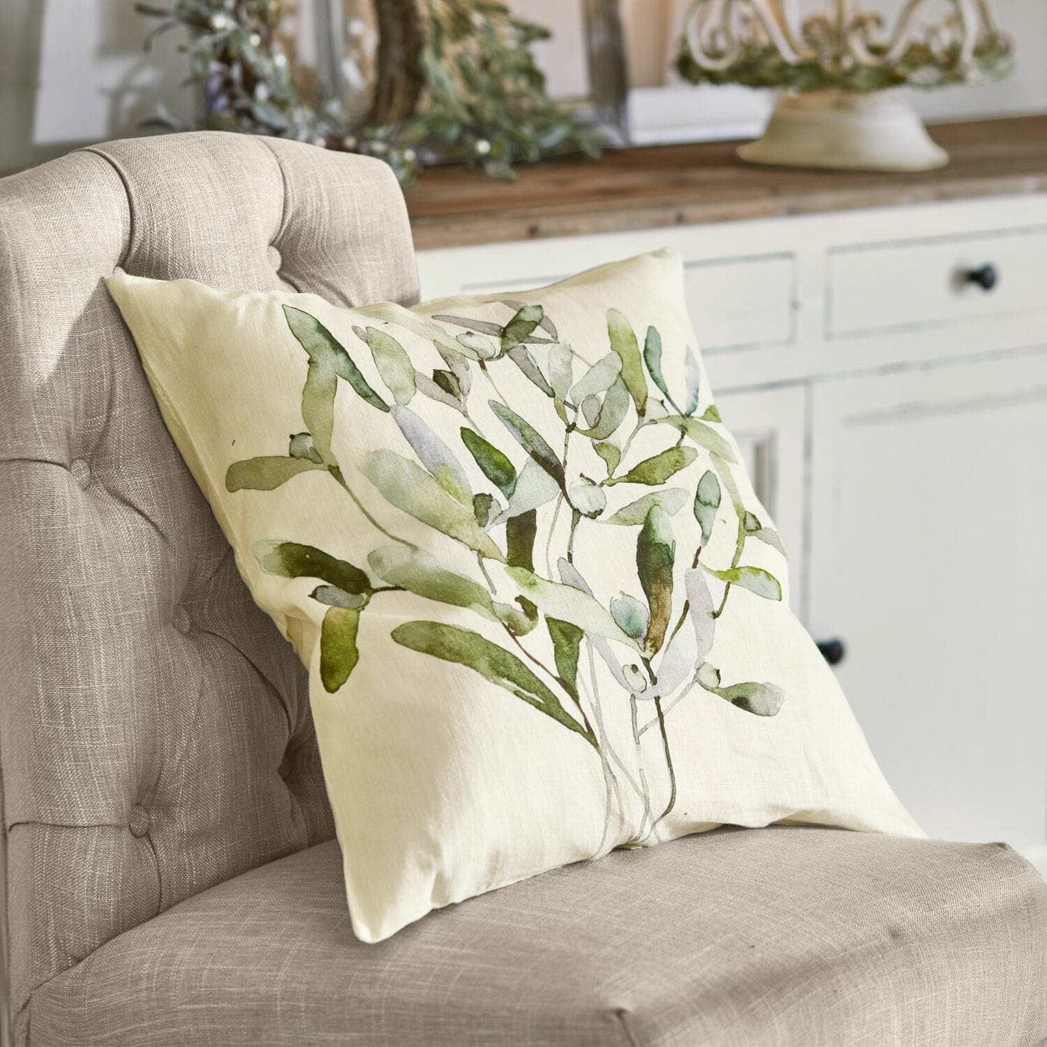 Kissenhülle Mistletoe Beige Dekokissen mit grünem Blattmuster auf grauem Stuhl in natürlichem Wohnstil