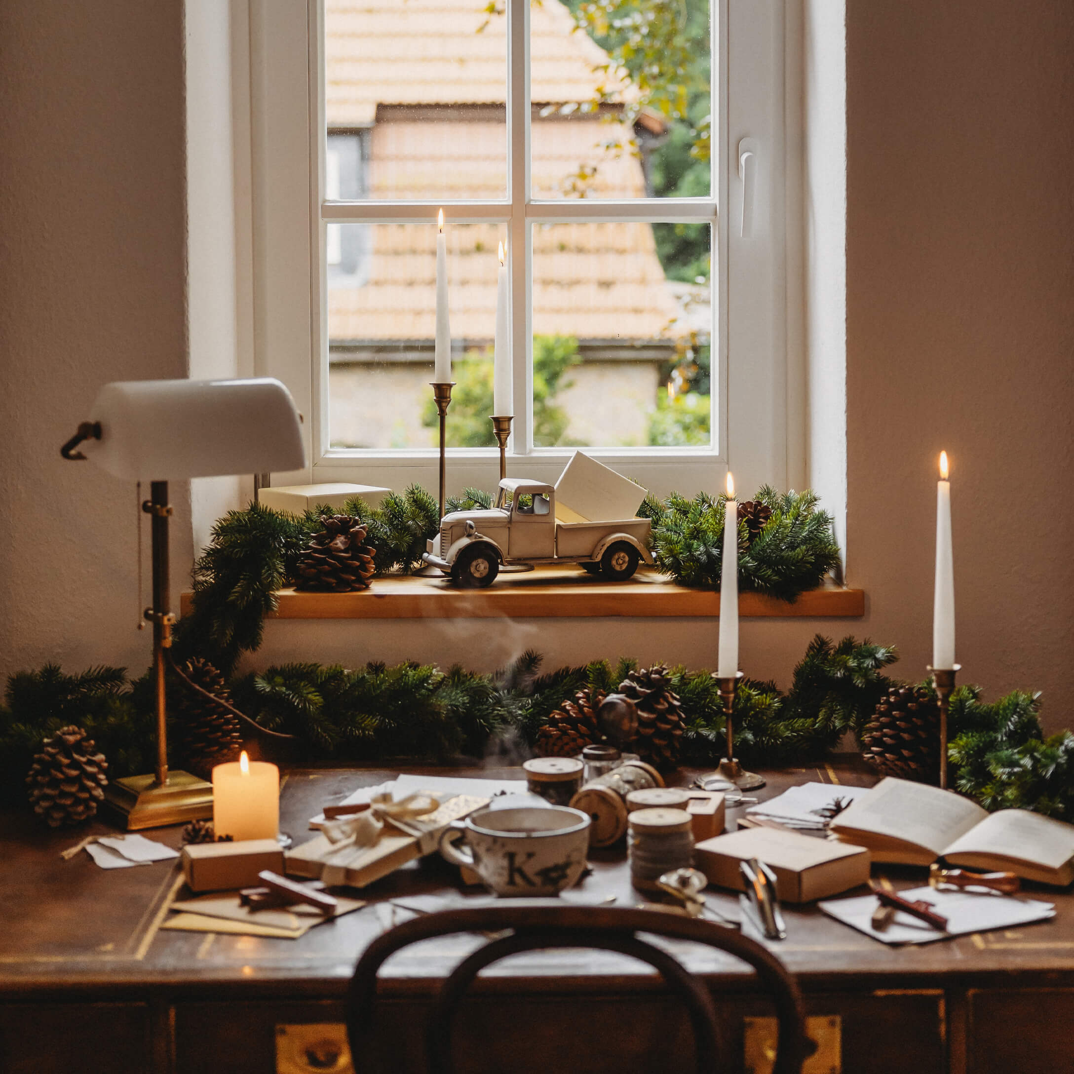 Rustikaler Holztisch mit Weihnachtsdekoration und Kerzen am Fenster mit Blick auf Dachziegel