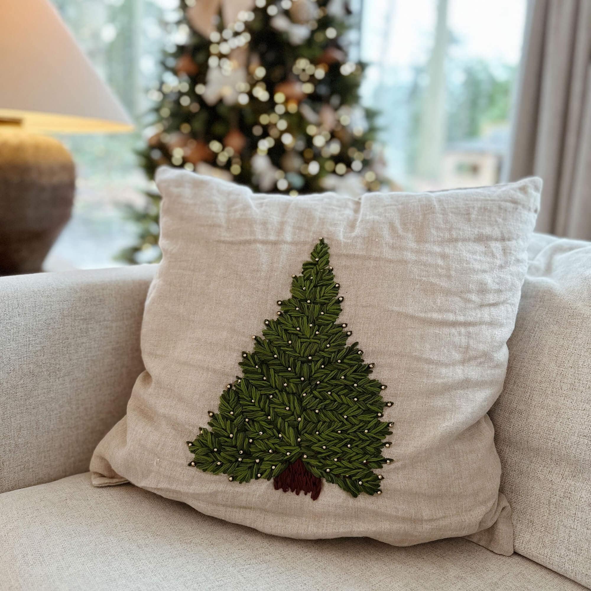Beige Leinenkissen mit grünem Tannenbaum-Stickmuster und braunem Stamm auf Sofa im Wohnzimmer