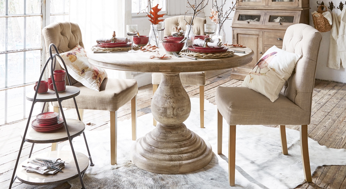 Heller Holztisch mit rundem Tischblatt und beige gepolsterte Stühle in gemütlichem Esszimmer mit Dekoration
