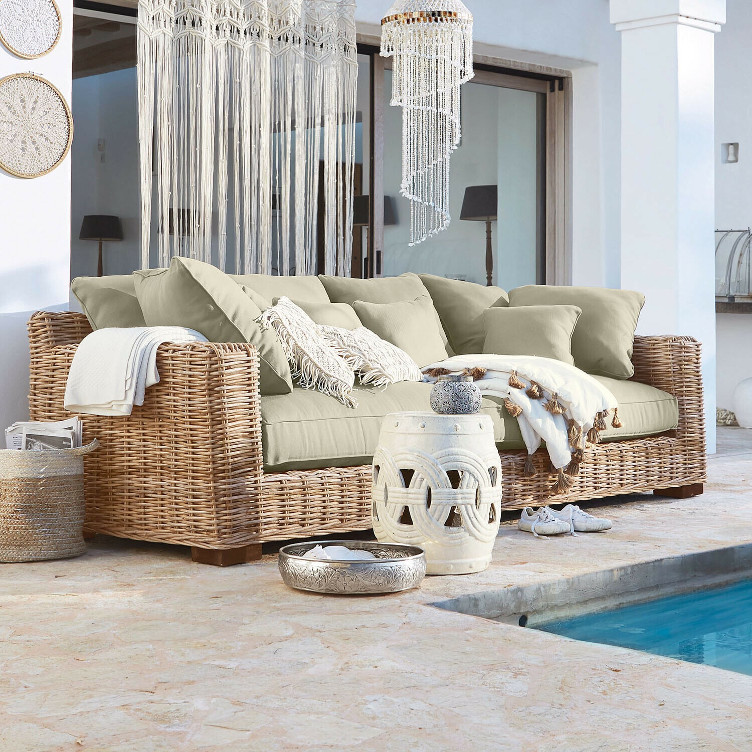 Rattansofa mit beigen Kissen und Boho-Dekorationen neben dem Pool im Außenbereich