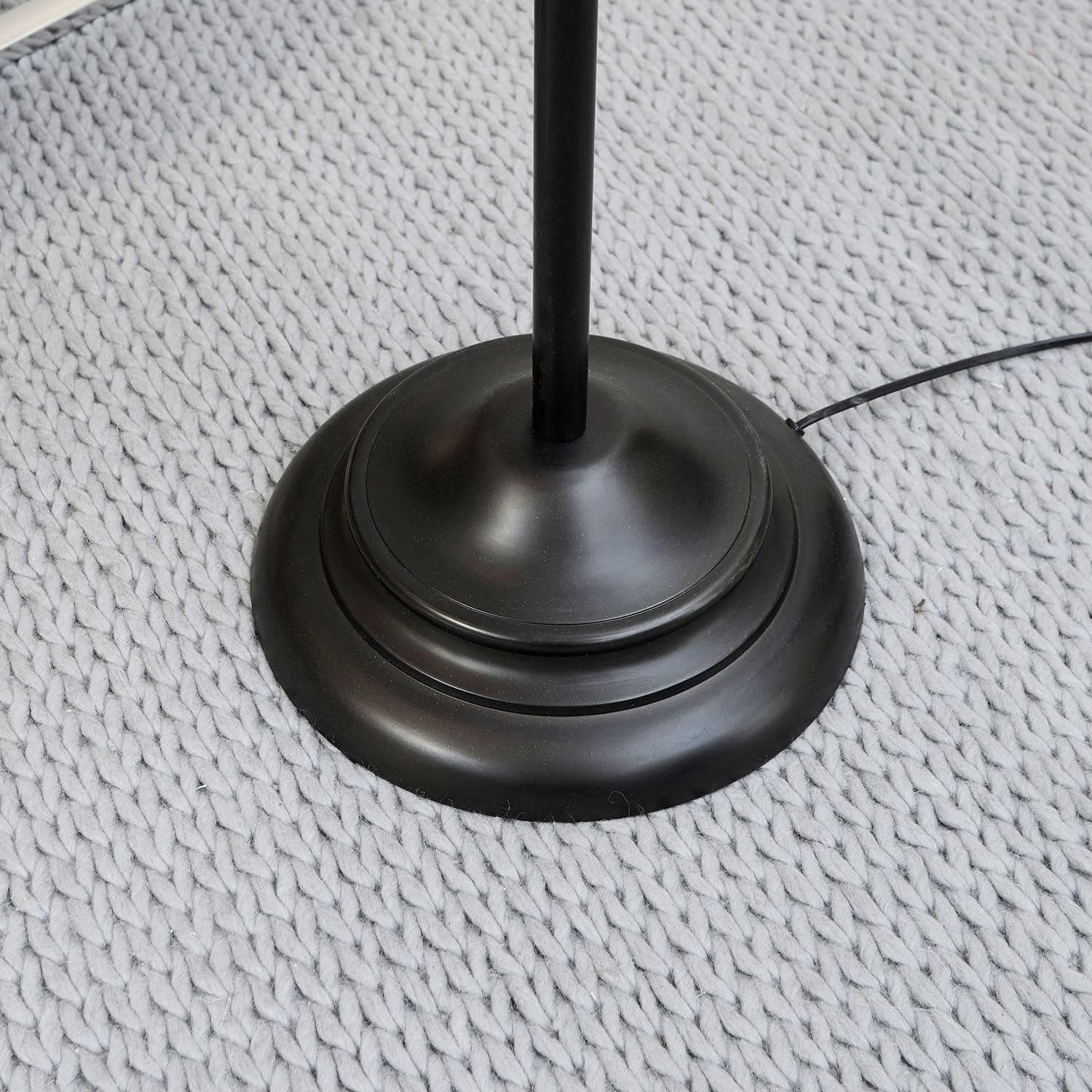 Schwarze Metalllampe mit runder Basis auf grauem Strickteppich, moderner Stil