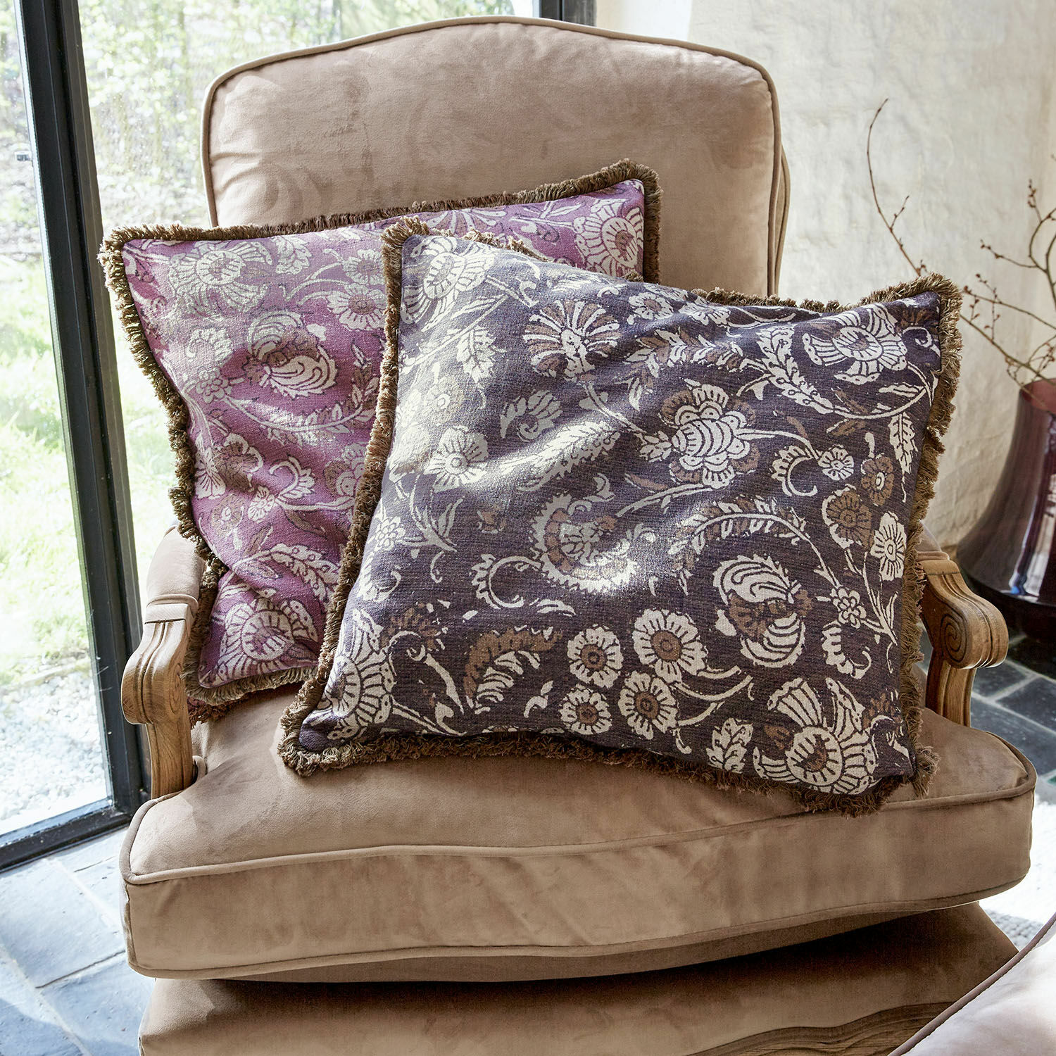 Kissenhülle 2er Set Lalluga Zwei dekorative Kissen mit floralem Muster in Violett und Grau auf einem beigen Sessel