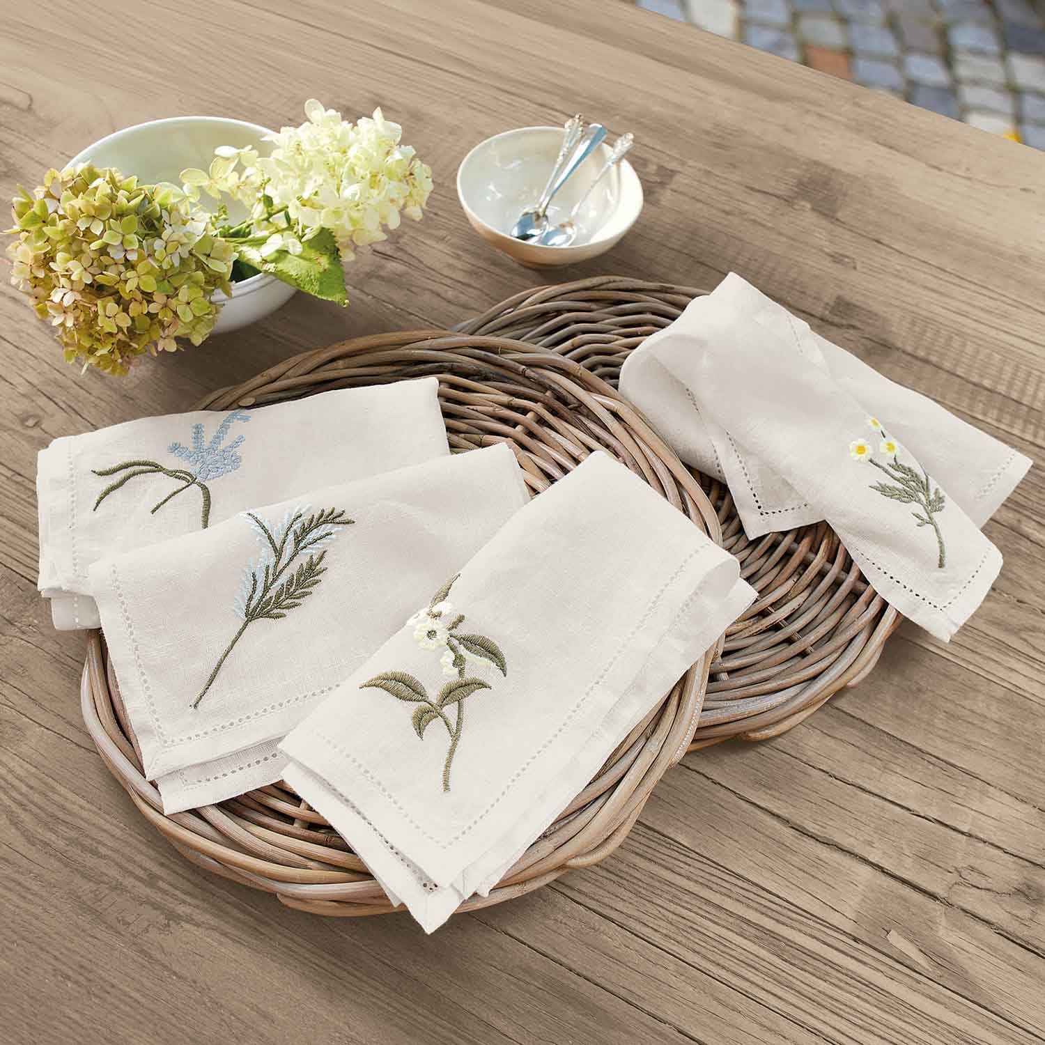Leinenservietten cremefarben mit Blumenstickerei auf Weidenkorb auf Holztisch