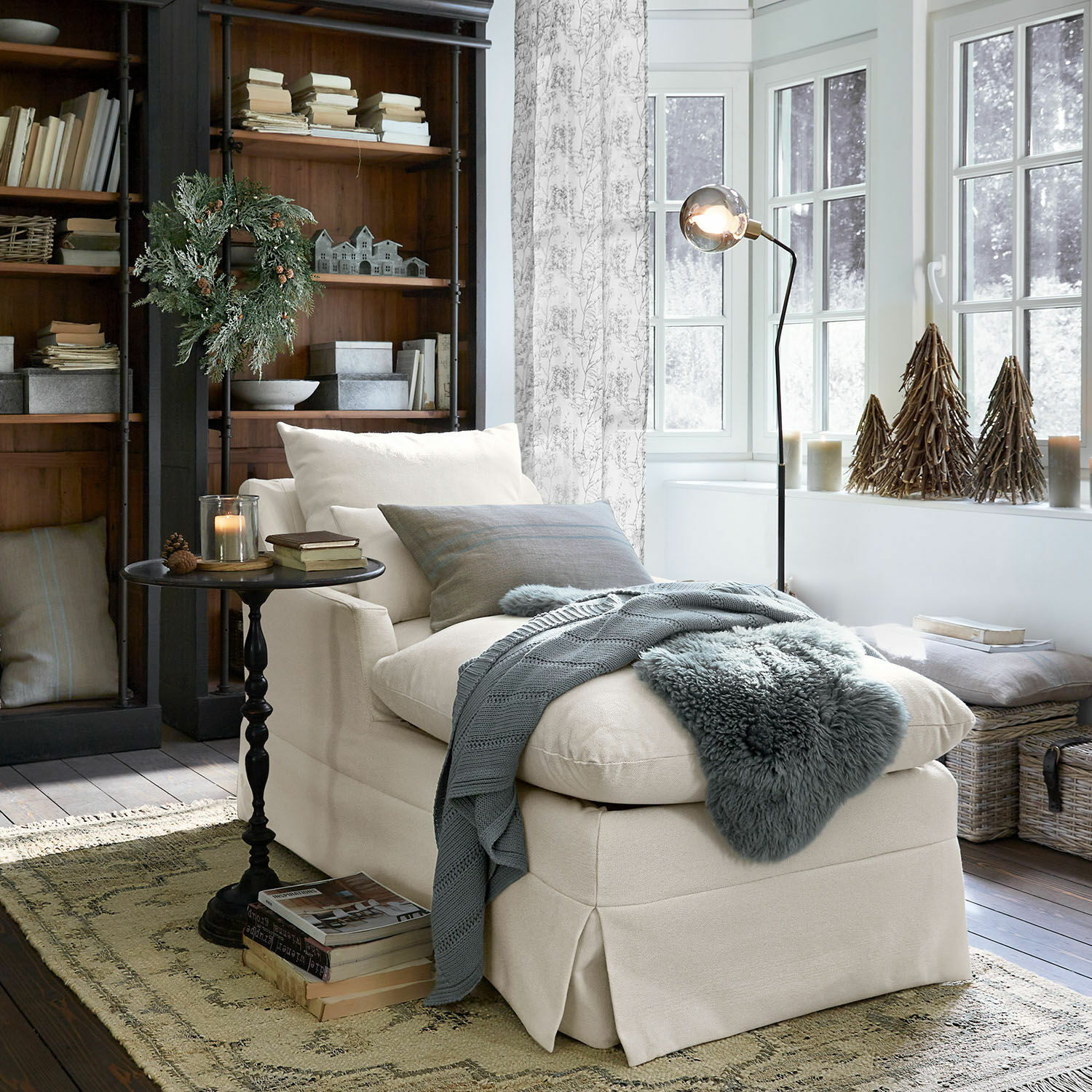 Beige gepolsterte Chaiselongue mit weichen Kissen und grauer Decke in gemütlichem Wohnzimmer mit Holzregal