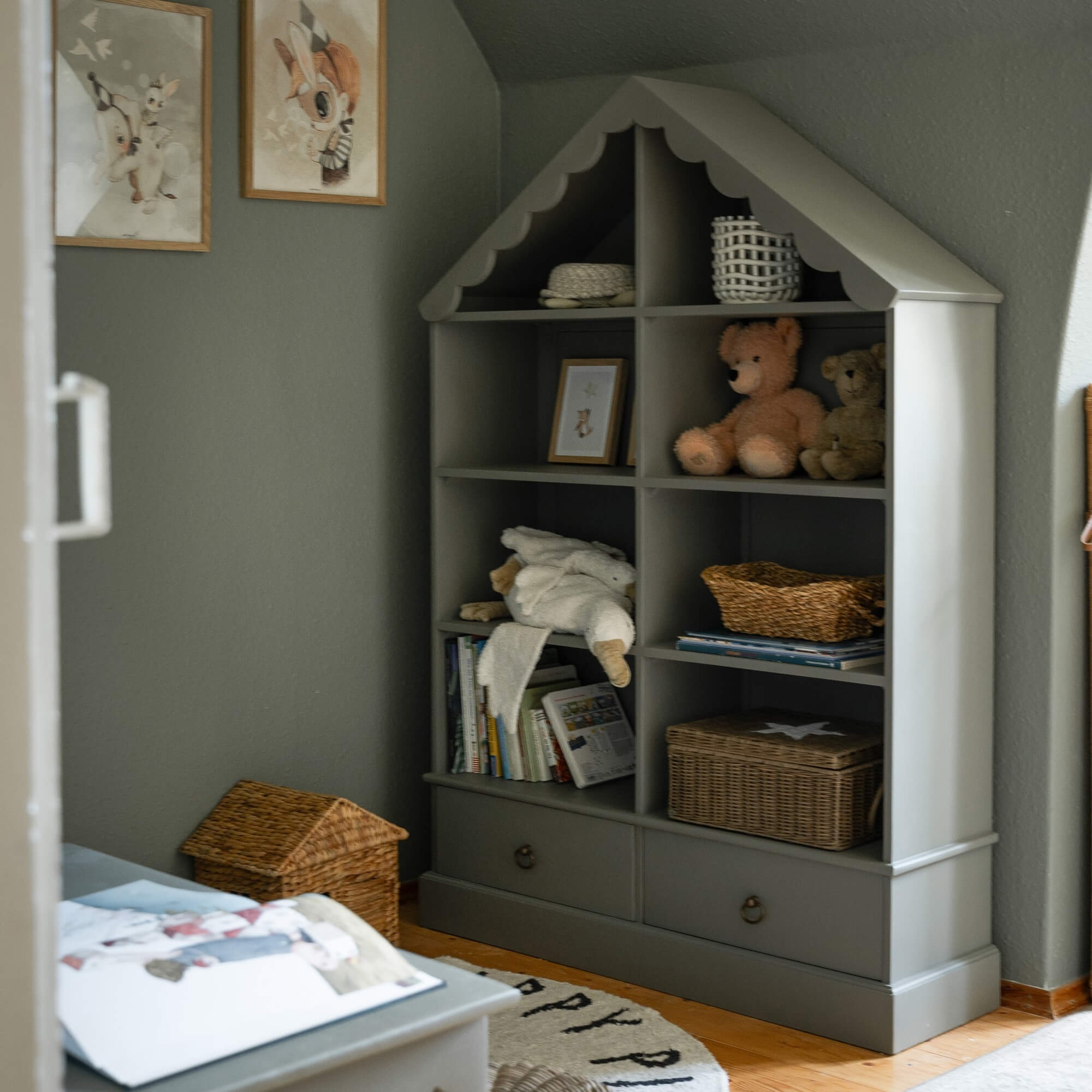 Graues Holzregal in Hausform mit Kuscheltieren und Körben im Kinderzimmer