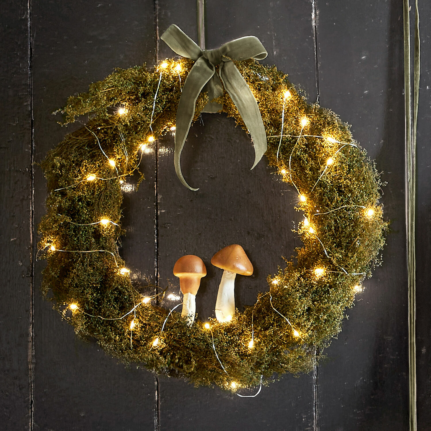 Mooskranz mit zwei Pilzen und warmweißer LED-Lichterkette an dunklem Hintergrund, Weihnachtsdeko