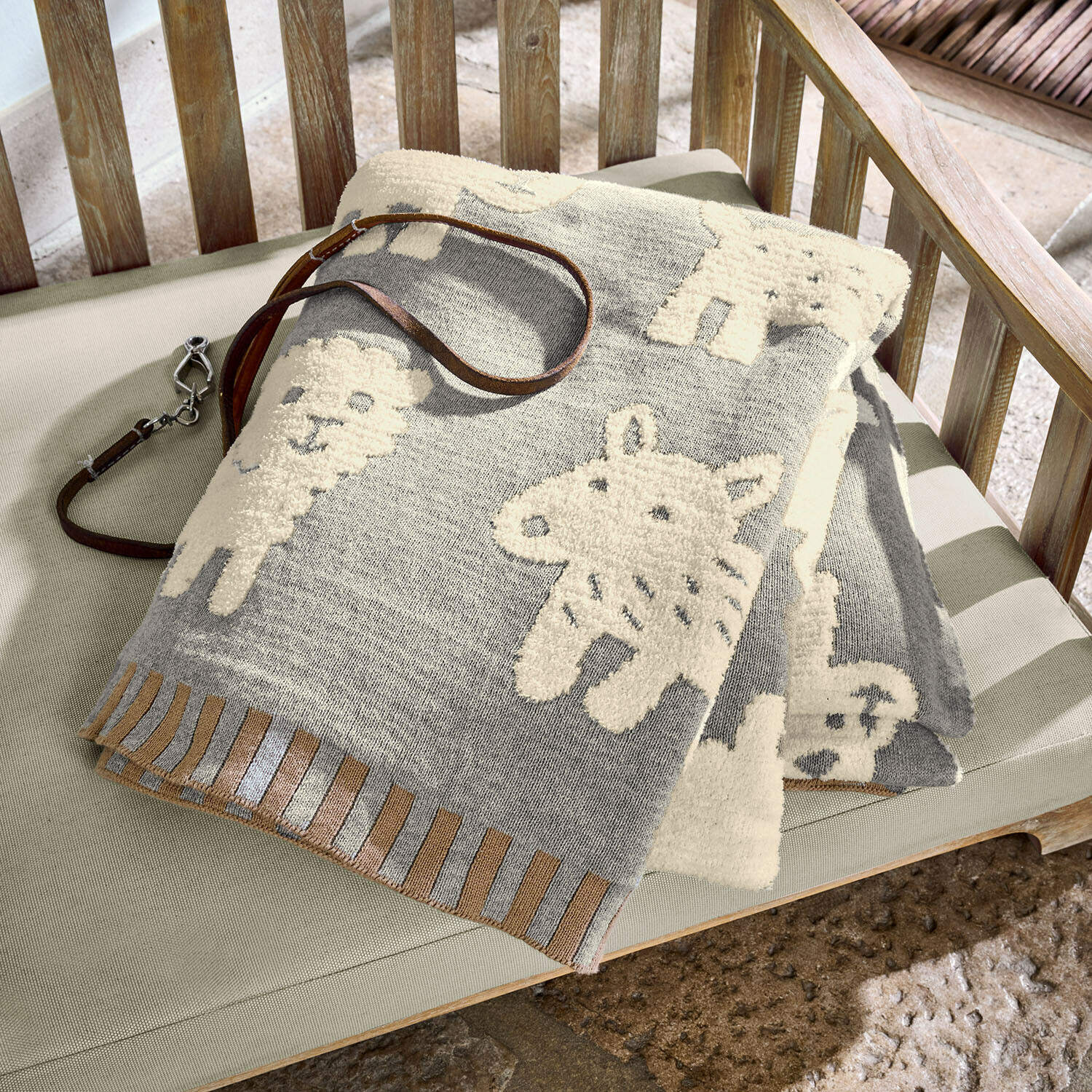 Hundedecke Fluffido Graue Baumwolldecke mit cremefarbenen Tiermotiven auf Holzbank, dekorative Kuscheldecke