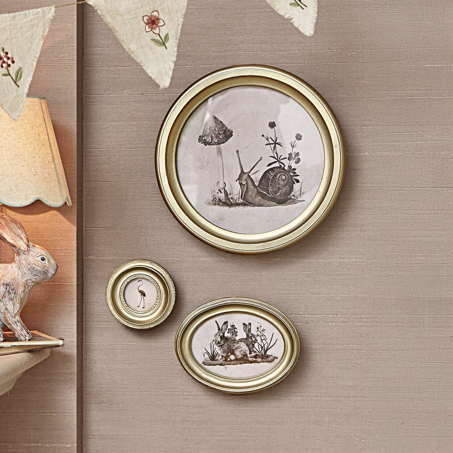 Bild 3er Set Atriana Drei goldene Bilderrahmen mit schwarz-weißen Tier- und Pflanzenillustrationen an beiger Wand.