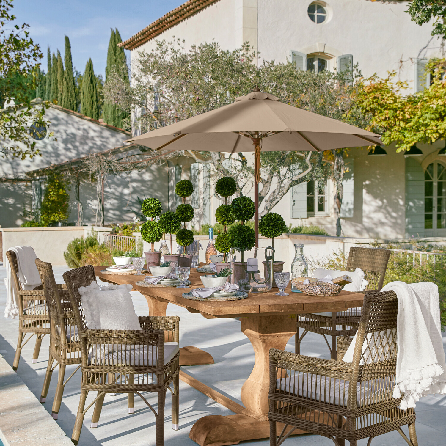 Sonnenschirm Brent Großer Holzgarten-Tisch mit Rattanstühlen und beigem Sonnenschirm auf sonniger Terrasse