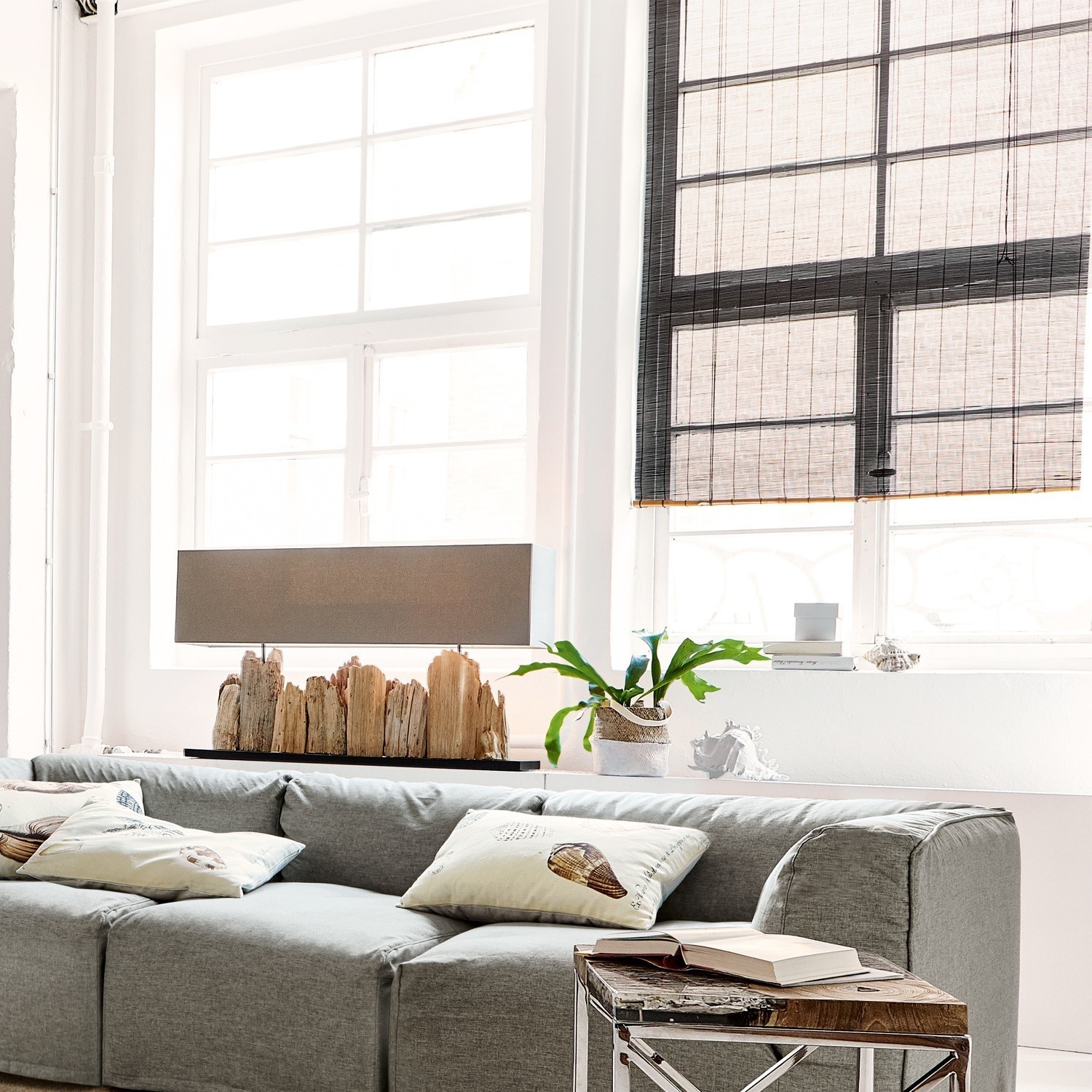 Moderne graue Couch mit Kissen und Holztisch in hellem Wohnzimmer mit Lampe und Pflanze