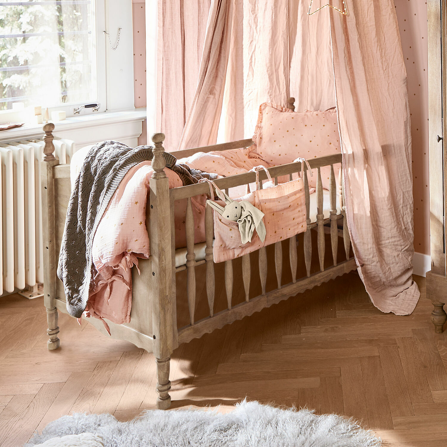 Kinderbett aus Holz mit rosa Bettwäsche und Vorhang, weicher Teppich auf Parkettboden